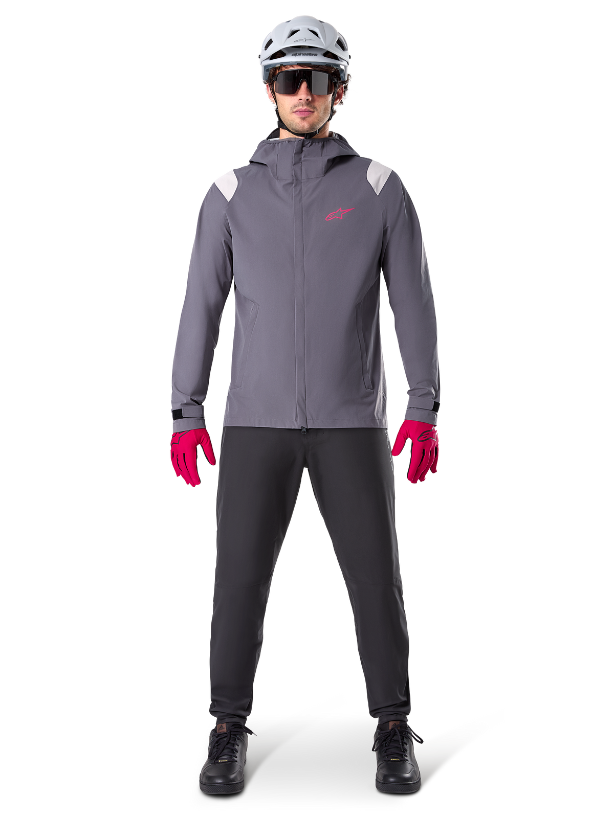 Alpinestars A-Dura Regenjas, mountainbike jas, donker titaniumgrijs met roze logo, gedragen met grijze MTB-helm en felroze handschoenen, beschermend 2,5-laags membraanontwerp voor fietsen in nat weer