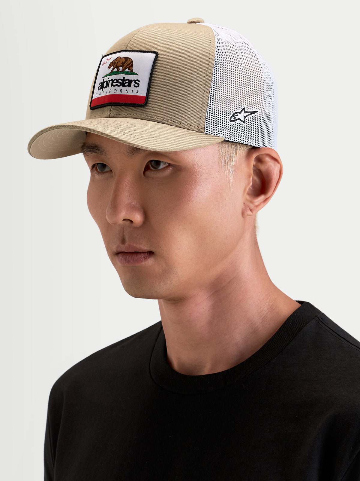 Casquette Alpinestars Cali 2.0, casquette trucker sportswear en khaki et blanc, portée par un modèle, avec visière incurvée, couronne structurée en sergé et empiècement avant