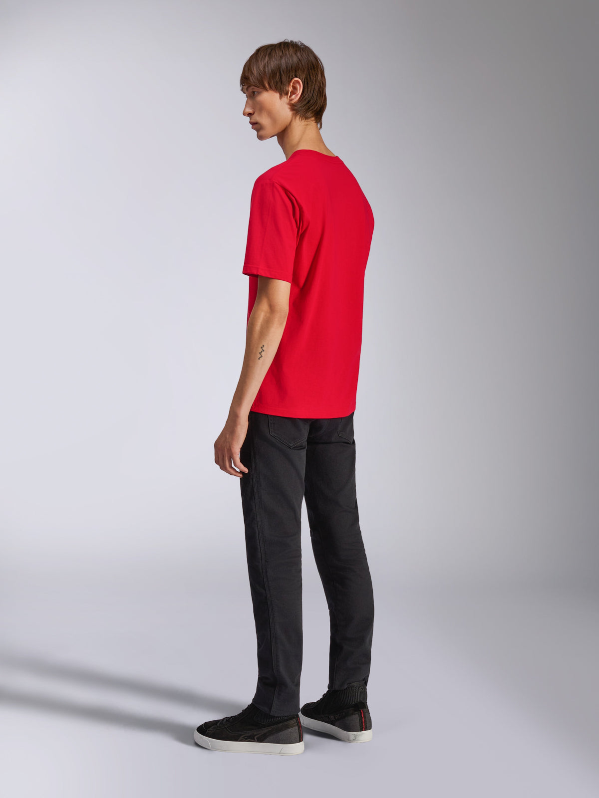 Alpinestars Ageless Shadow CSF Tee, kurzärmeliges T-Shirt, Rot, Rückansicht am Modell, getragen mit schwarzer Hose und Sneakern, lässige vom Motorsport inspirierte Streetwear