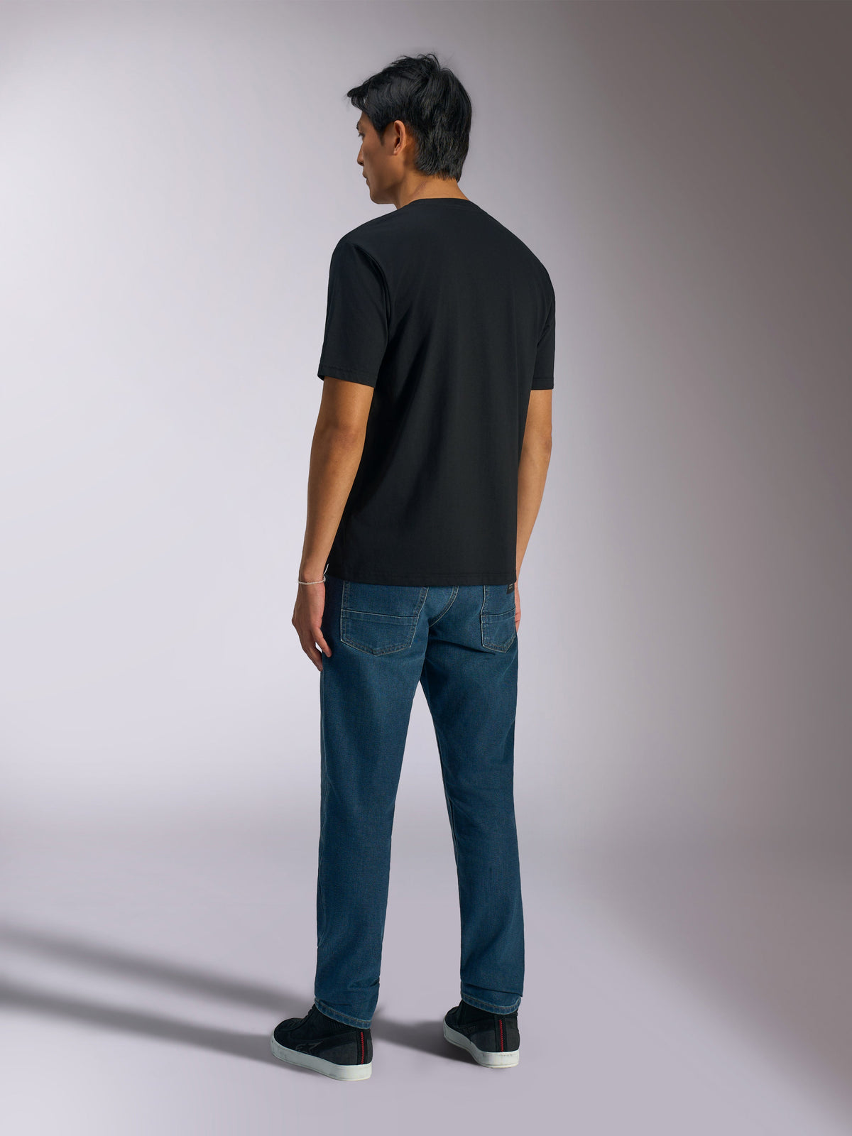 Alpinestars Ageless Shadow CSF Tee, T-shirt met korte mouwen, zwart, achteraanzicht, gedragen met een blauwe spijkerbroek en zwarte sneakers, casual streetwear geïnspireerd op de motorsport