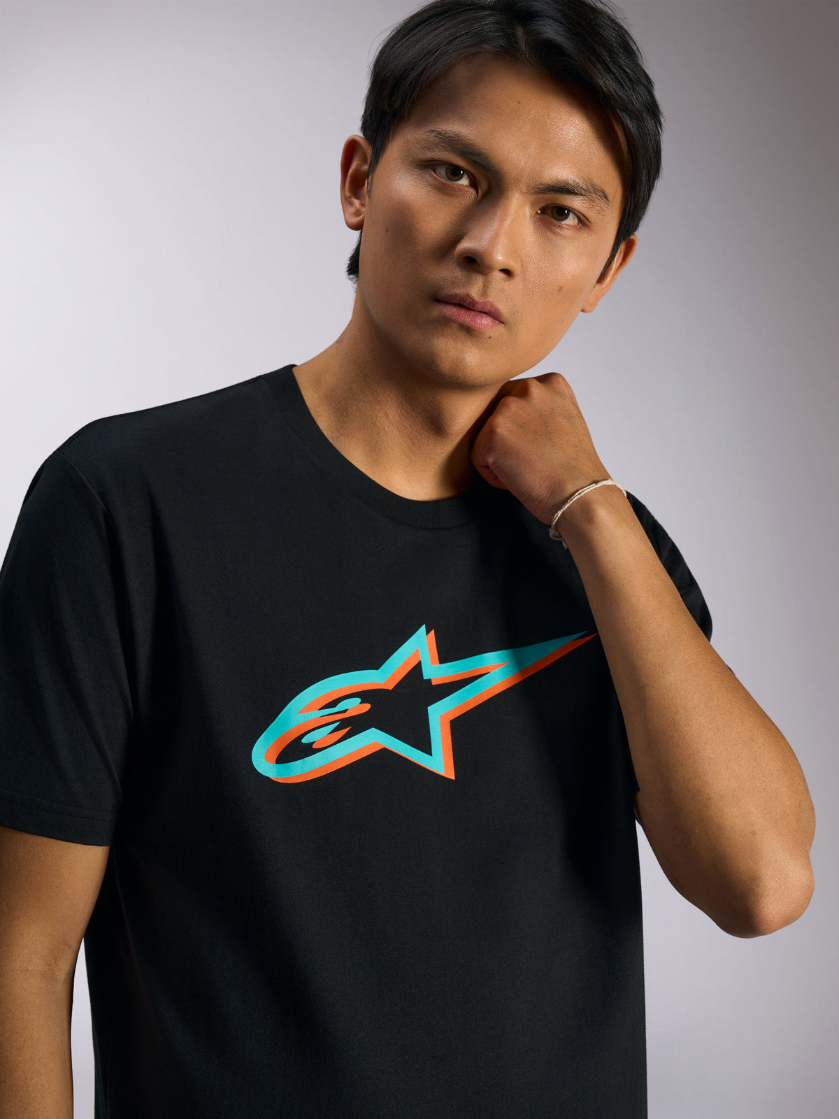 Alpinestars Ageless Shadow CSF Tee, T-shirt met korte mouwen, zwart met turquoise en oranje Shadow-logo, gedragen door model, casual motorsport-geïnspireerde streetwear