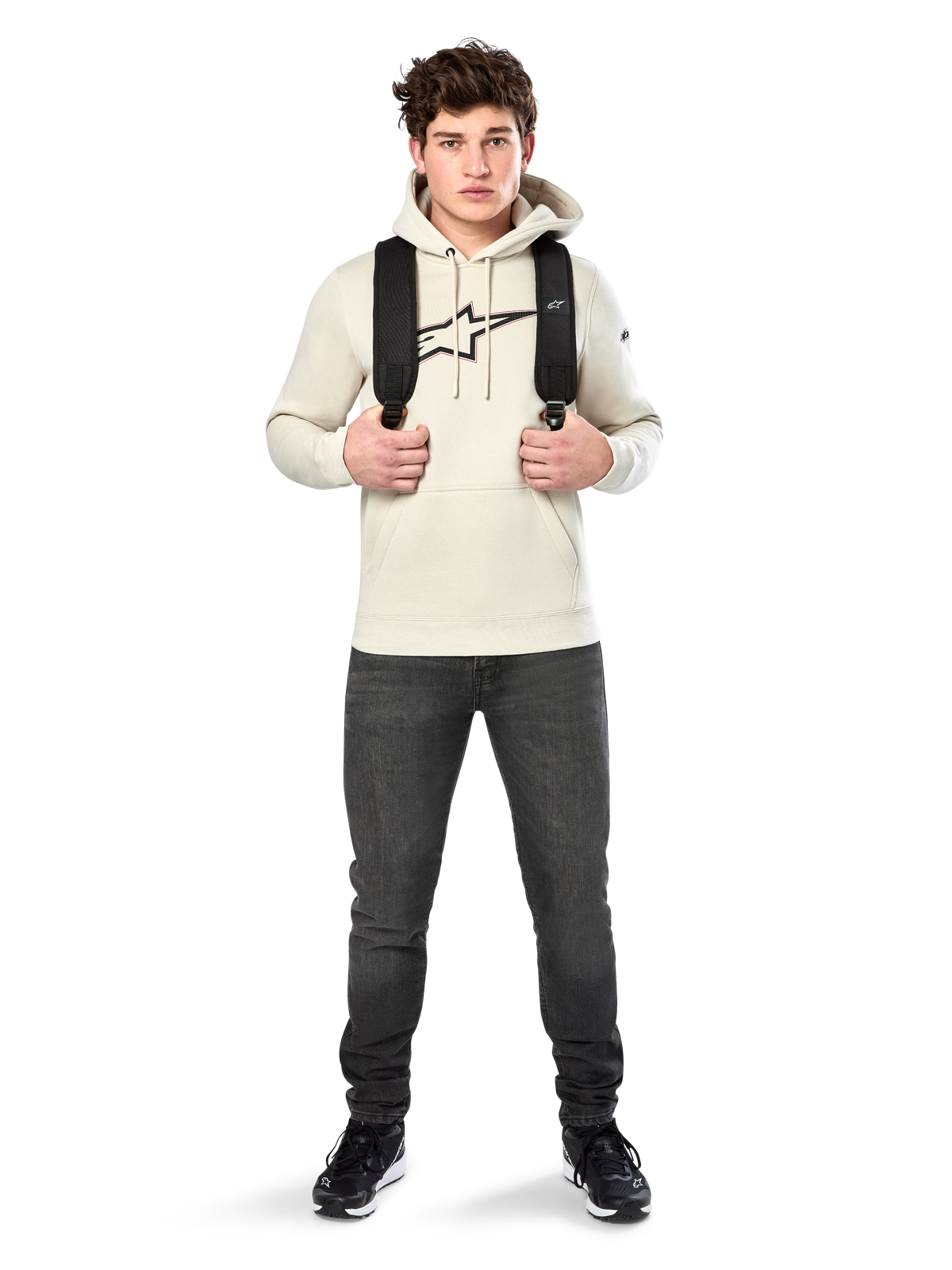 Sweat à capuche Insignia Alpinestars, streetwear décontracté, pull en polaire blanc cassé, logo aspect fibre de carbone avec contour rouge, capuche à cordon de serrage, poche kangourou, porté par un mannequin avec un sac à dos noir et un jean gris foncé