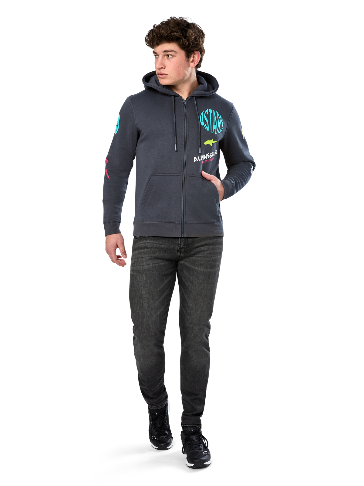 Alpinestars Variegate Hoodie, Fleece-Hoodie mit Reißverschluss, Gunmetal-Grau, getragen von einem Modell mit schwarzen Jeans und Sneakern, mit türkisfarbenem 'ASTARS'-Branding und bunten Logo-Grafiken auf Ärmeln und Brust, lässige Motorsport-Streetwear