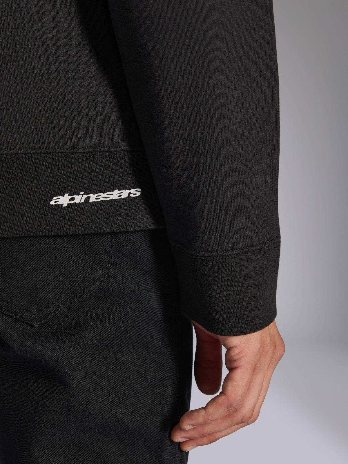 Alpinestars Positive Crew, zwarte pullover sweatshirt, detailopname van de geribbelde zoom en mouwboord met wit Alpinestars-logo, hoogwaardige stoftextuur, casual op motorsport geïnspireerde sportkleding