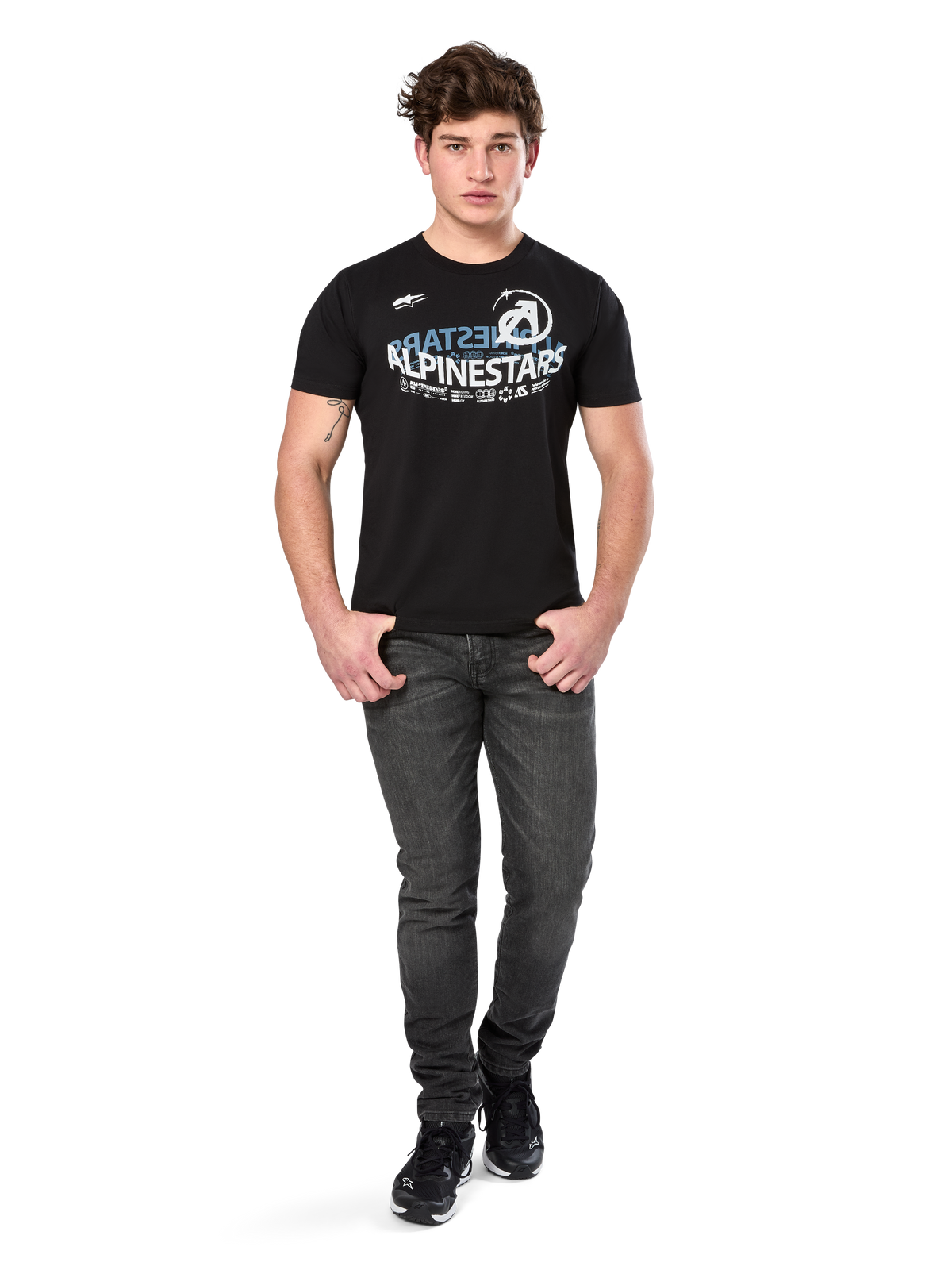 Alpinestars Semicircle CSF Tee, Kurzarm-T-Shirt, Schwarz, weißes und hellblaues geschwungenes Grafik-Design auf der Brust, getragen von einem Modell mit dunkelgrauen Jeans und schwarzen Sneakern, lässige Motorsport-Streetwear