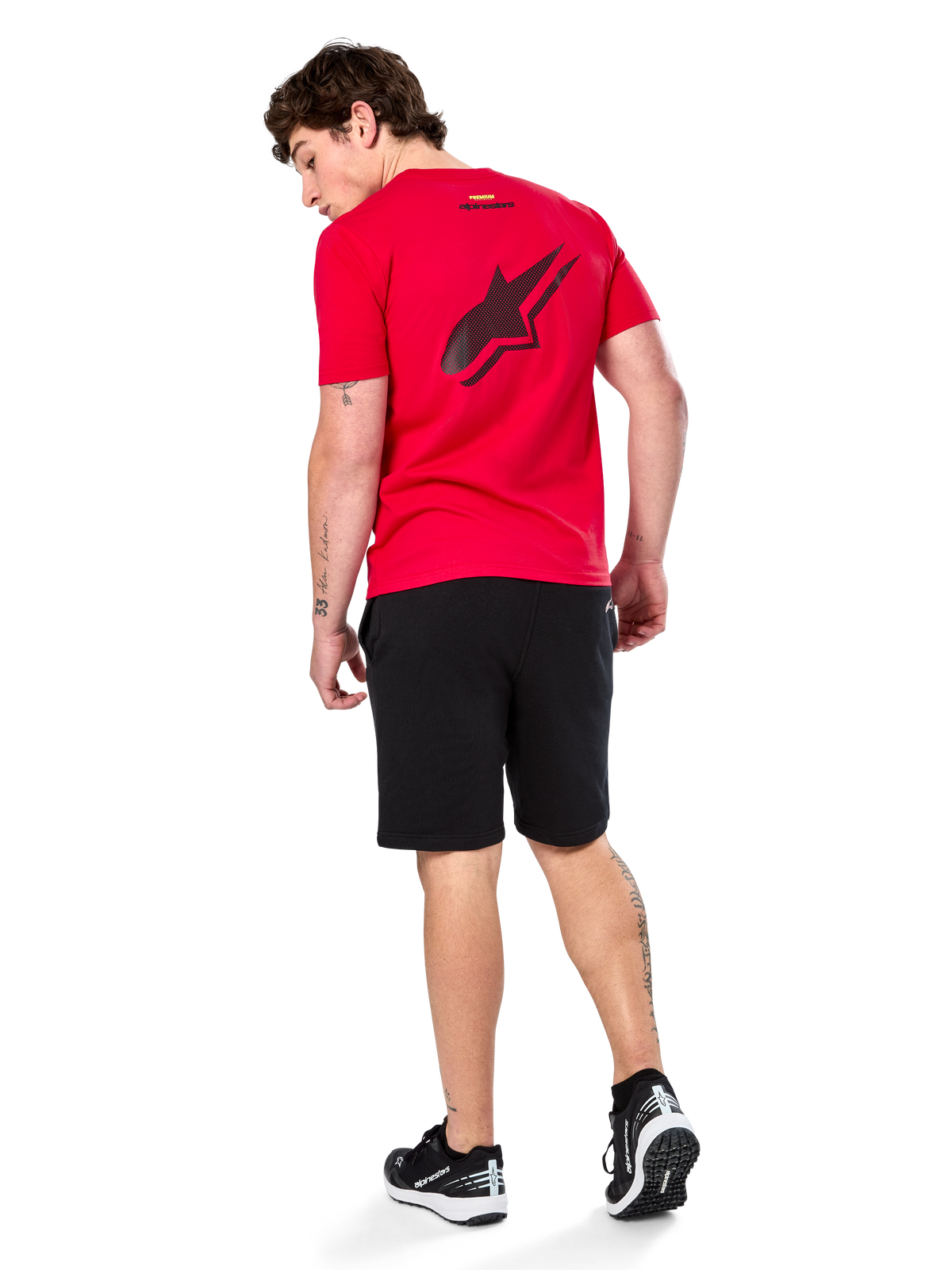 Alpinestars Formulate Csf Tee, Kurzarm-T-Shirt, Rot, großes schwarzes perforiertes Astars-Logo auf der Rückseite, getragen mit schwarzen Shorts und Sneakern, lässige vom Motorsport inspirierte Streetwear