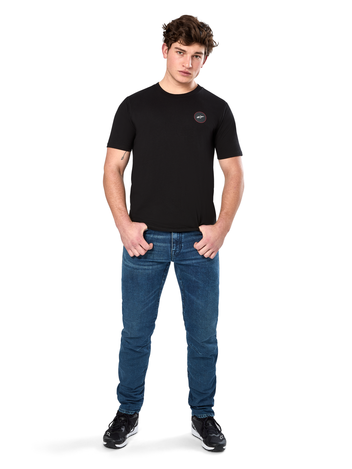 Alpinestars Dot Carbon CSF Tee, T-shirt met korte mouwen, zwart, klein rond Astars Dot-logo op de borst, gedragen met blauwe jeans en zwarte sneakers, casual motorsport streetwear