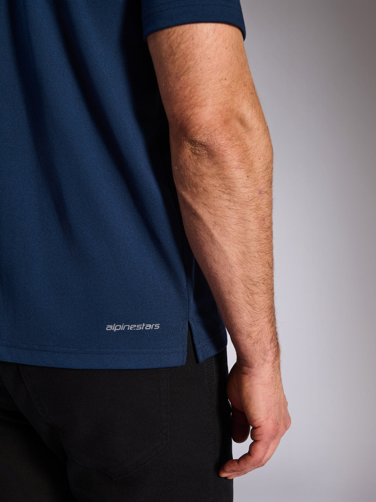 Alpinestars Impetus Sport Polo, Navy, close-up van de onderste zoom met het Alpinestars-woordmerk en zijsplit, mock-mesh gebreide textuur, casual motorsport sportkleding
