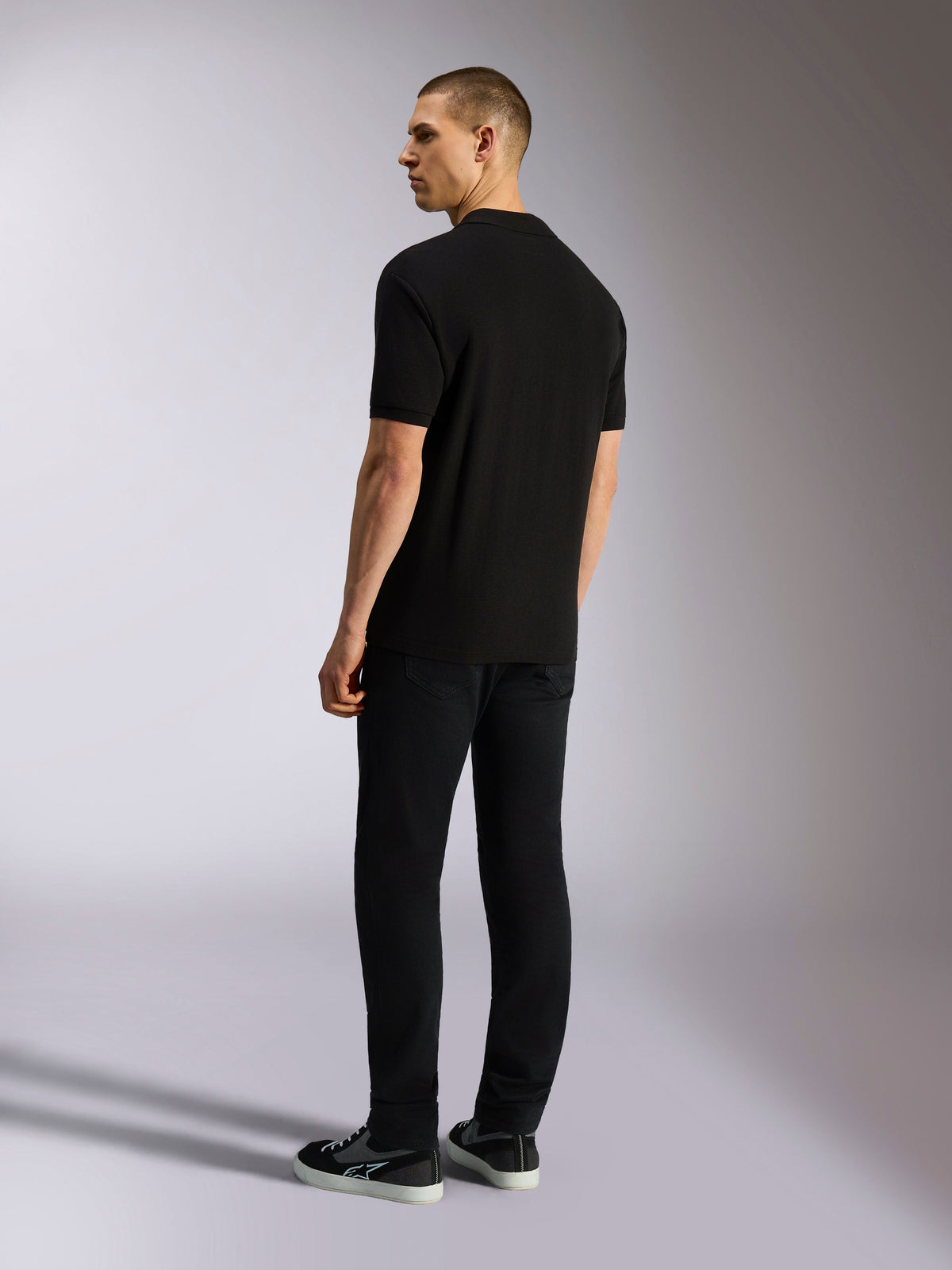 Alpinestars Endeavor Classic Polo, piqué poloshirt met korte mouwen, zwart, achteraanzicht van een mannelijk model met een zwarte broek en sneakers, casual motorsport-geïnspireerde streetwear