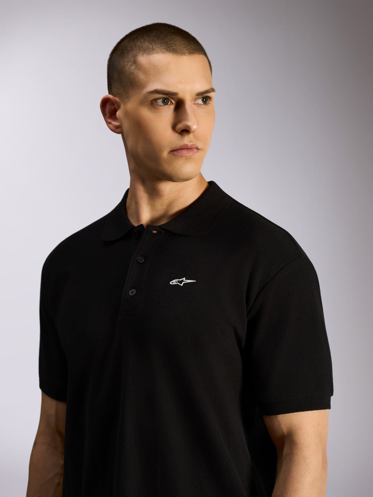 Alpinestars Endeavor Classic Polo, zwart piqué poloshirt gedragen door een mannelijk model, klein wit Astars-logo op de borst, sluiting met drie knopen en geribde kraag, casual motorsport streetwear