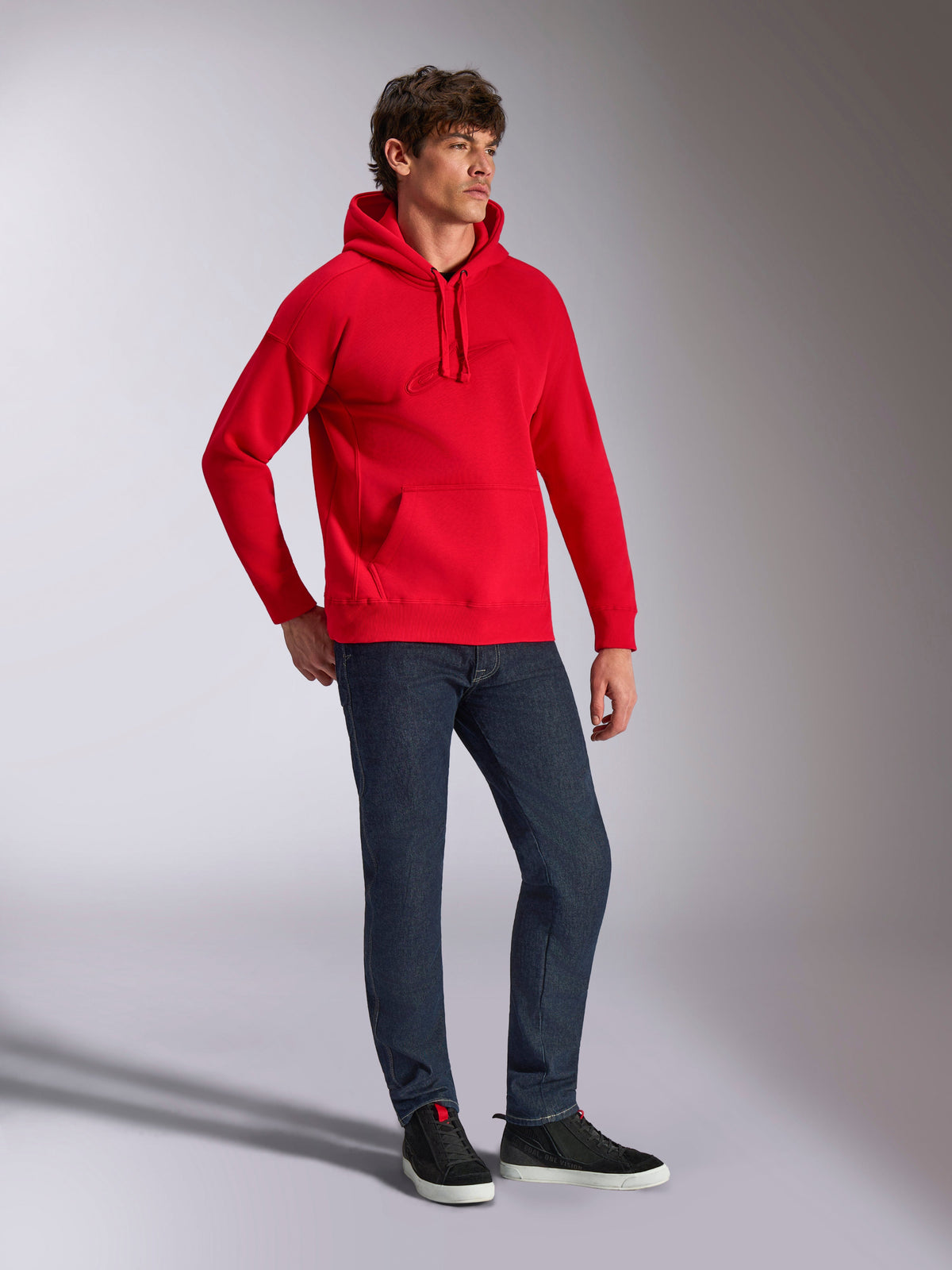 Alpinestars Emergent Oversized Hoodie, Rot, Fleece-Kapuzenpullover mit tonaler 3D-Stickerei, Oversized-Passform, getragen von einem Model mit dunkelblauer Jeans und schwarzen Sneakern, lässige vom Motorsport inspirierte Streetwear