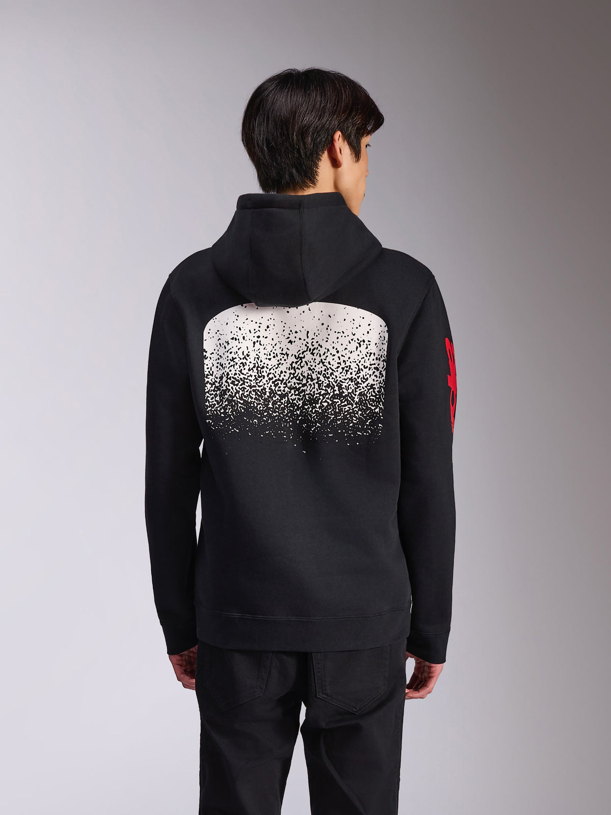 Alpinestars Obsessed Hoodie, vue arrière d'un sweat à capuche noir en polaire, arborant un large graphique blanc moucheté en dégradé MX au dos et des logos Alpinestars rouges sur les manches, style streetwear décontracté inspiré des sports mécaniques