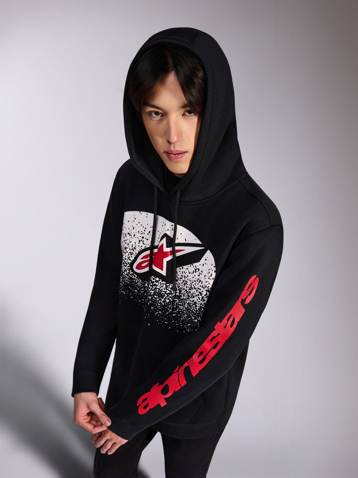 Alpinestars Obsessed Hoodie, sweat à capuche noir en polaire, logo Astars rouge et blanc sur le devant avec dégradé MX blanc effet vieilli, inscription Alpinestars rouge sur la manche, capuche à cordon de serrage, streetwear décontracté inspiré du sport automobile