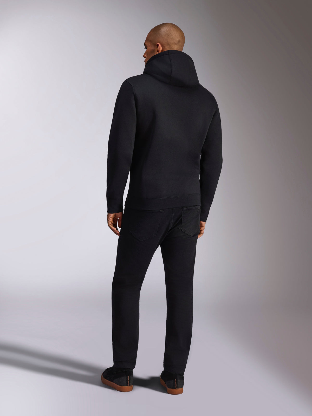 Alpinestars Ellipsoid Hoodie, lässige Sportbekleidung, einfarbiger schwarzer Fleece-Kapuzenpullover, Rückansicht, lange Ärmel und Rippsaum, kombiniert mit schwarzer Hose, modernes vom Motorsport inspiriertes Design