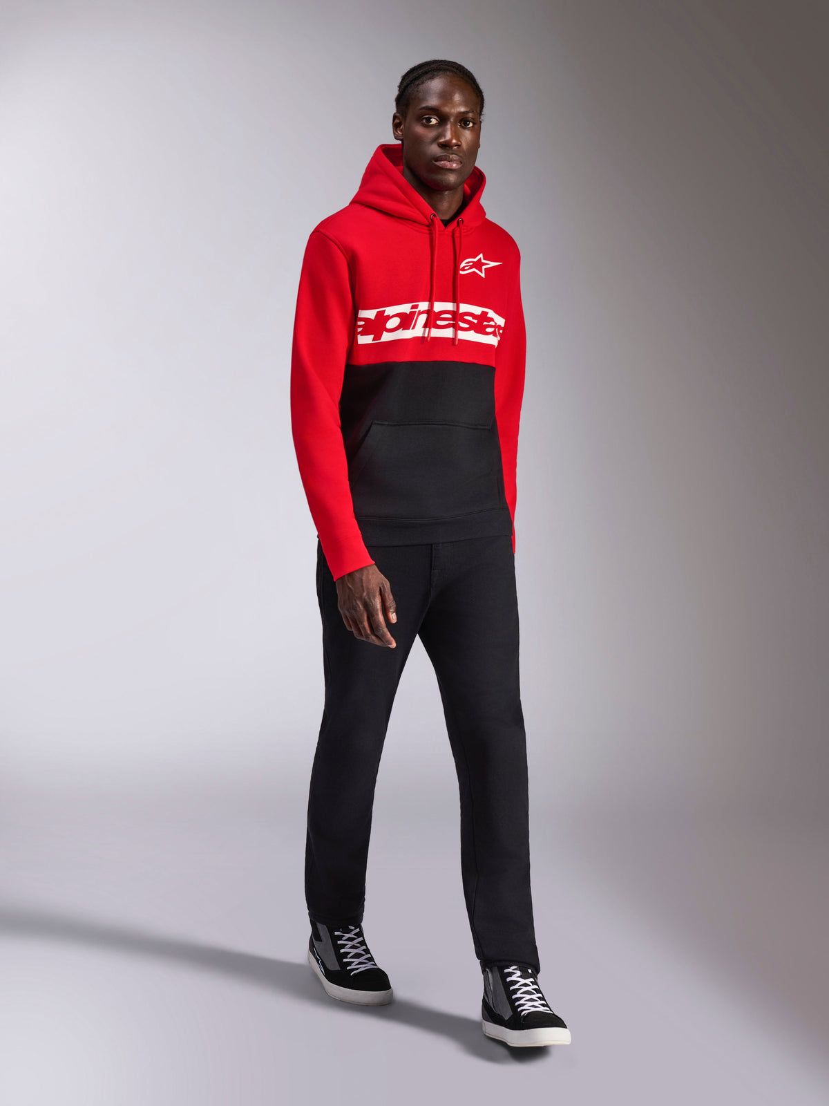 Alpinestars Parallel Hoodie, casual sportkleding, rood en zwart kleurgeblokkeerd ontwerp, met een wit Alpinestars woordmerk en sterlogo op de borst, gedragen met zwarte broek en sneakers, moderne op motorsport geïnspireerde look