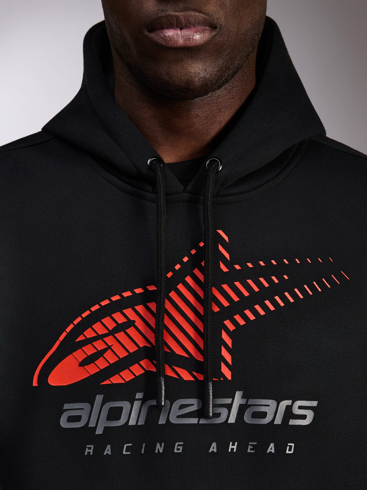 Alpinestars Pulse Hoodie, zwarte pullover hoodie, close-up van de borst met rood Astars-logo met speed line fade en zilveren merkdetails, zwarte trekkoorden met gedipte uiteinden, casual motorsport streetwear