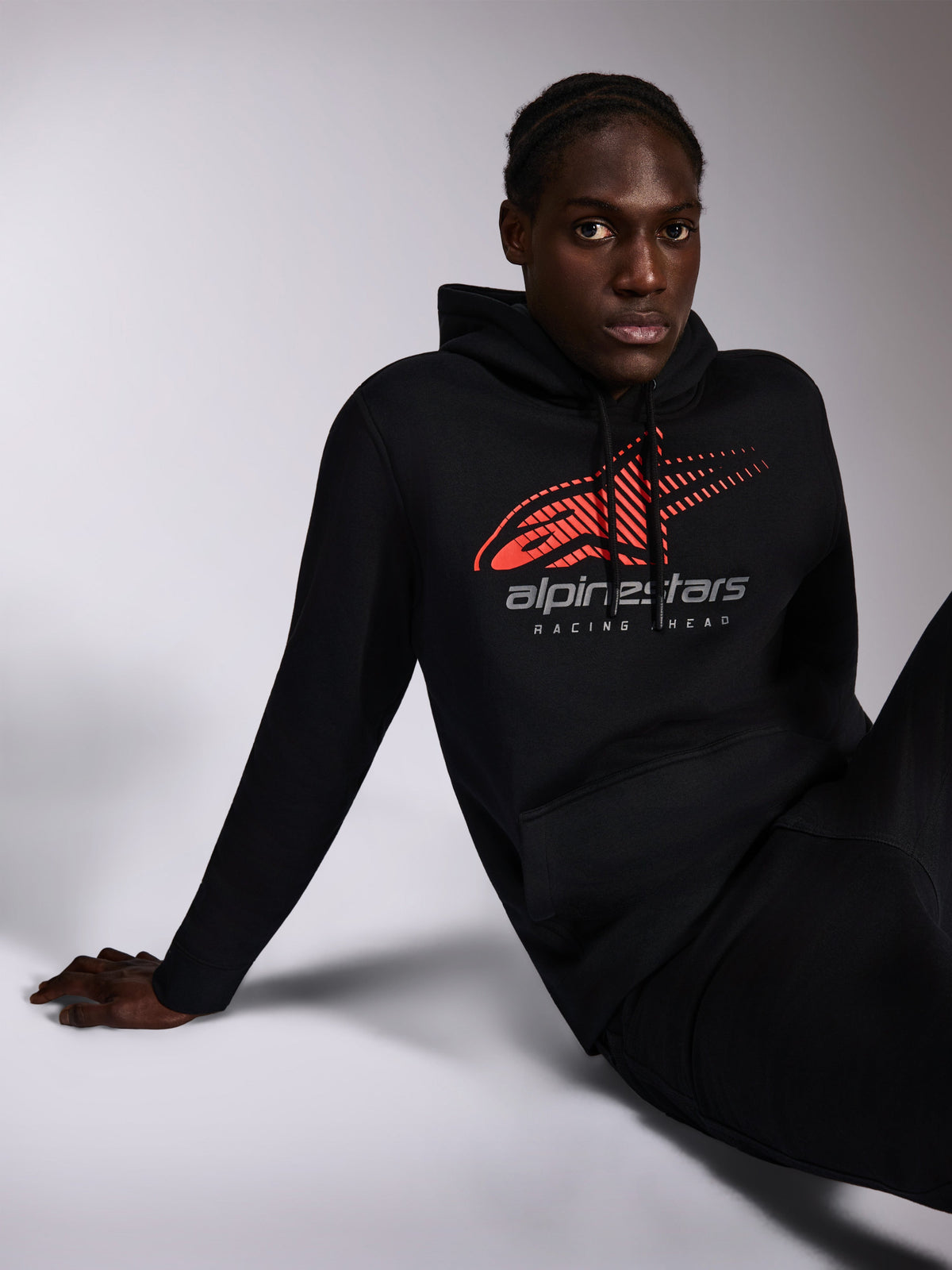 Alpinestars Pulse Hoodie, zwarte casual streetwear gedragen door model, met rood Astars-logo met speed line fade en 'alpinestars RACING AHEAD' tekst op de borst, capuchon met trekkoord, lange mouwen, modern motorsport-geïnspireerd ontwerp