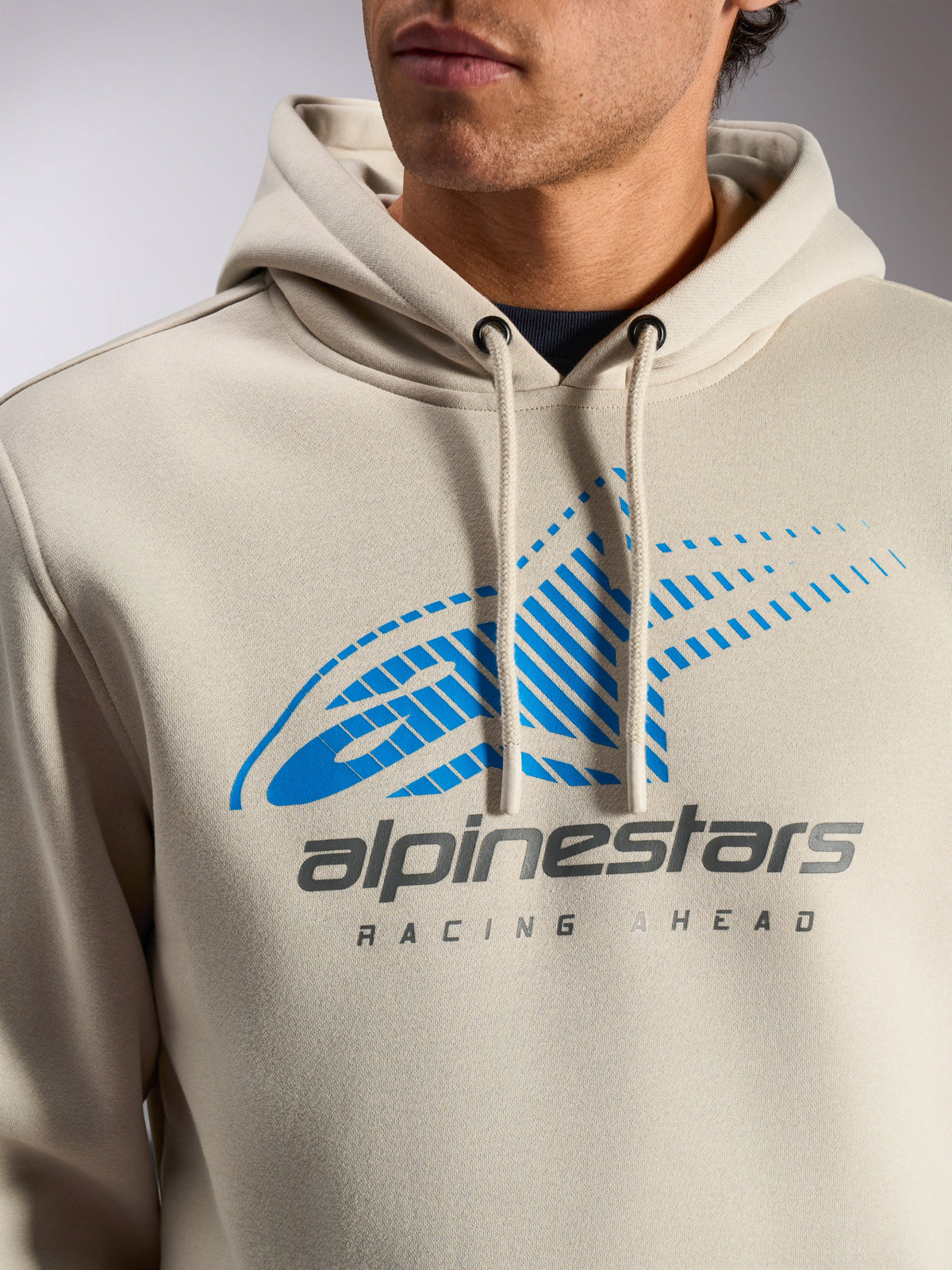 Sweat à capuche Pulse Alpinestars, pullover streetwear décontracté blanc cassé, gros plan sur la poitrine avec le logo Astars Combo bleu et gris, dégradé de lignes de vitesse et texte « Racing Ahead », capuche à cordon avec embouts trempés.