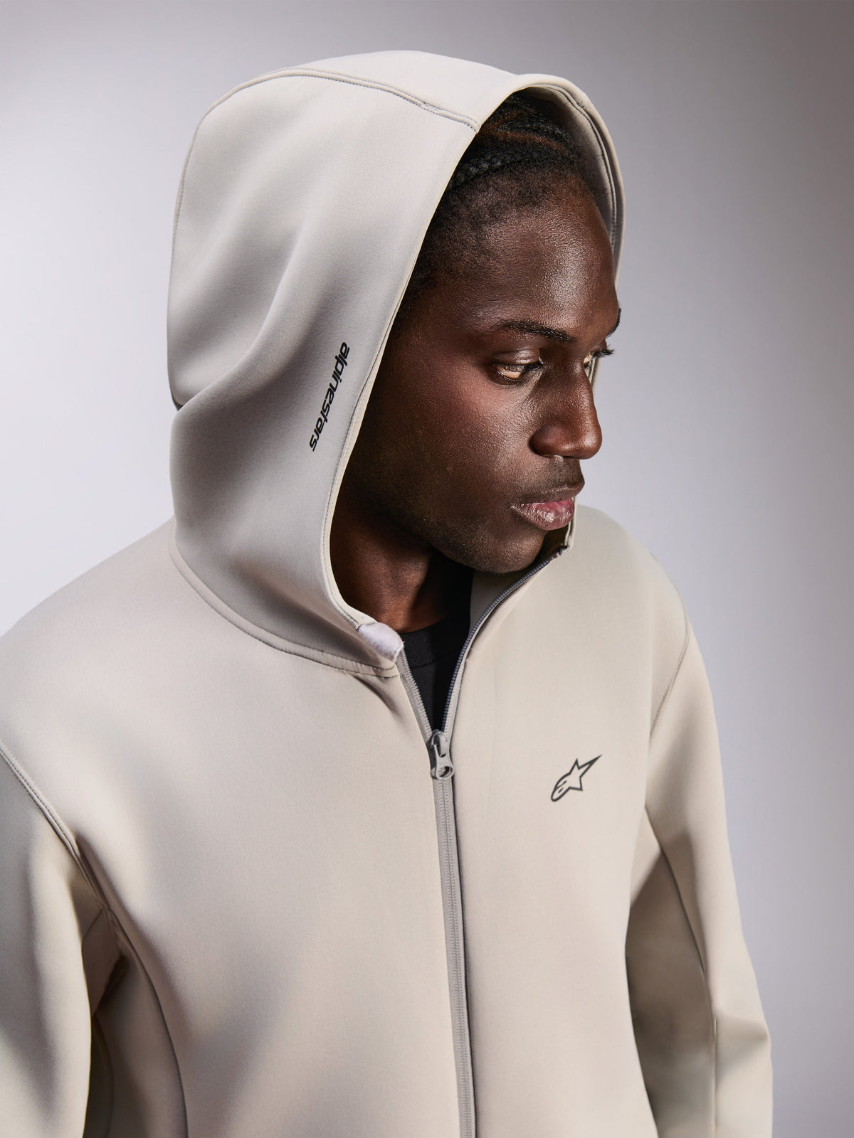 Alpinestars Cypher Hoodie, sweat à capuche zippé en polaire, gris ciment, porté avec la capuche relevée, avec logo Alpinestars sur la capuche et petit logo Astars sur la poitrine, streetwear décontracté inspiré du sport automobile