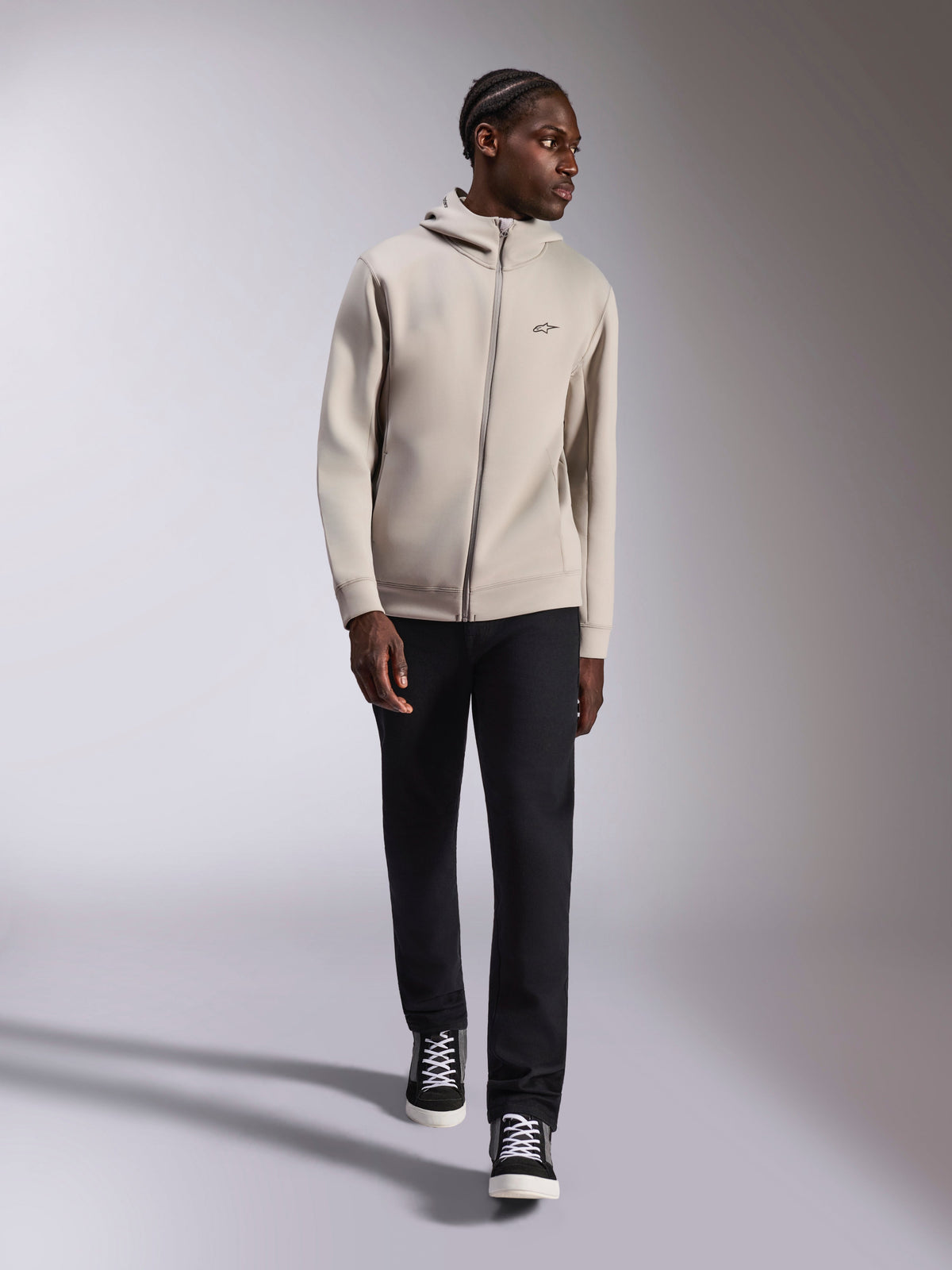 Sweat à capuche Alpinestars Cypher, hoodie zippé en polaire double face, Gris Ciment, porté par un mannequin avec un pantalon noir et des baskets noires et blanches, doté d'une capuche à col haut doublée de mesh et d'un petit logo Astars sur la poitrine, style streetwear décontracté moderne