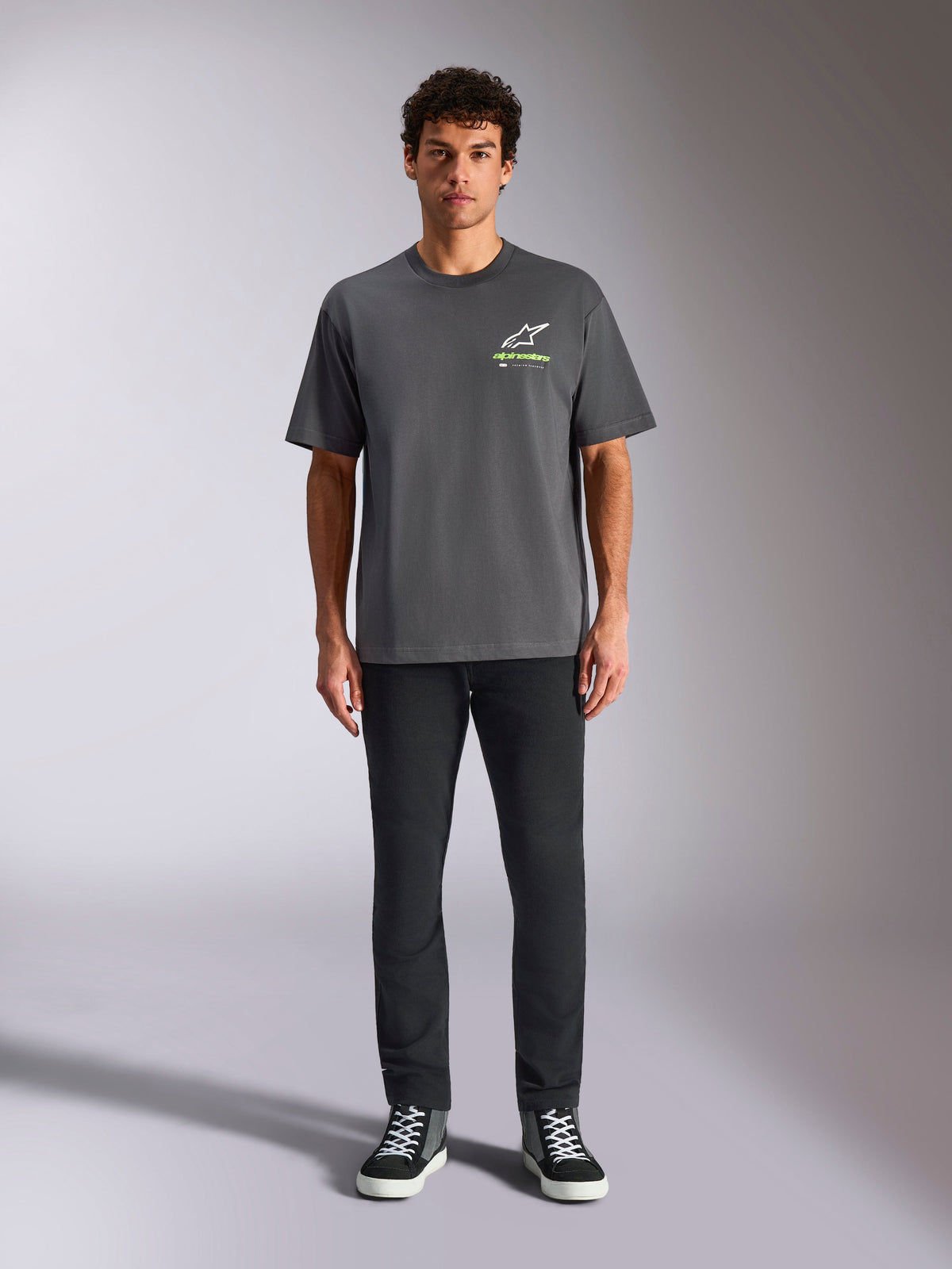 Alpinestars Overhang Oversized CSF Tee, T-shirt met korte mouwen, antracietgrijs, met een wit en limegroen Alpinestars-logo op de voorkant, gedragen door een model met een zwarte broek en sneakers, relaxte casual streetwear