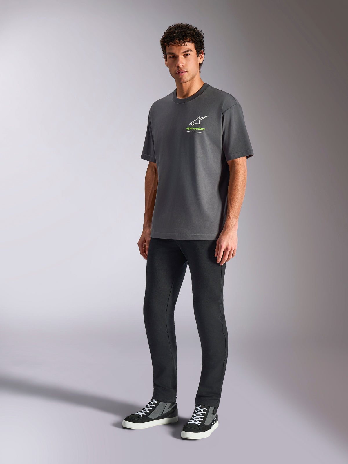 Alpinestars Overhang Oversized CSF Tee, T-shirt met korte mouwen, antracietgrijs, voorzien van wit Astars-logo en groene tekst op de borst, gedragen door model met zwarte broek en sneakers, ontspannen oversized pasvorm, casual motorsport streetwear
