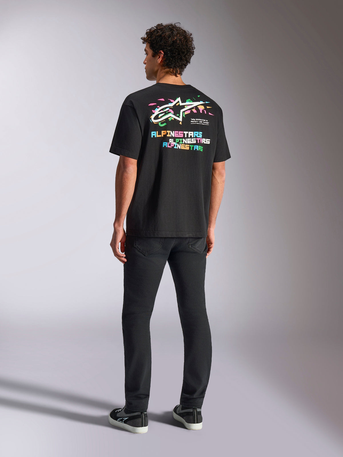 T-shirt Alpinestars Wild Oversized CSF, t-shirt à manches courtes, noir, présentant un grand graphisme multicolore au dos avec le logo Astars et un lettrage coloré, coupe surdimensionnée, porté avec un pantalon slim noir pour un look streetwear décontracté