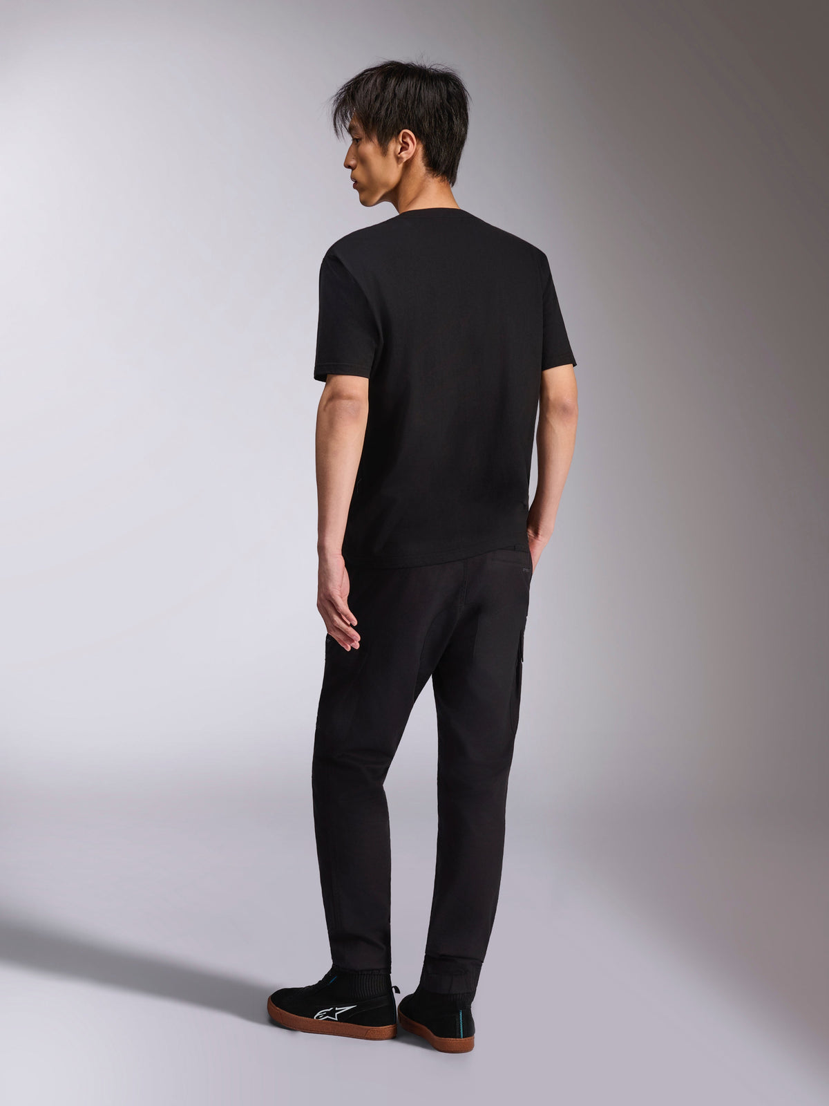 Alpinestars Noka CSF Tee, kurzärmeliges T-Shirt, Schwarz, Rückansicht am Modell, kombiniert mit schwarzer Hose und lässigen Sneakern, minimalistische Motorsport-Streetwear