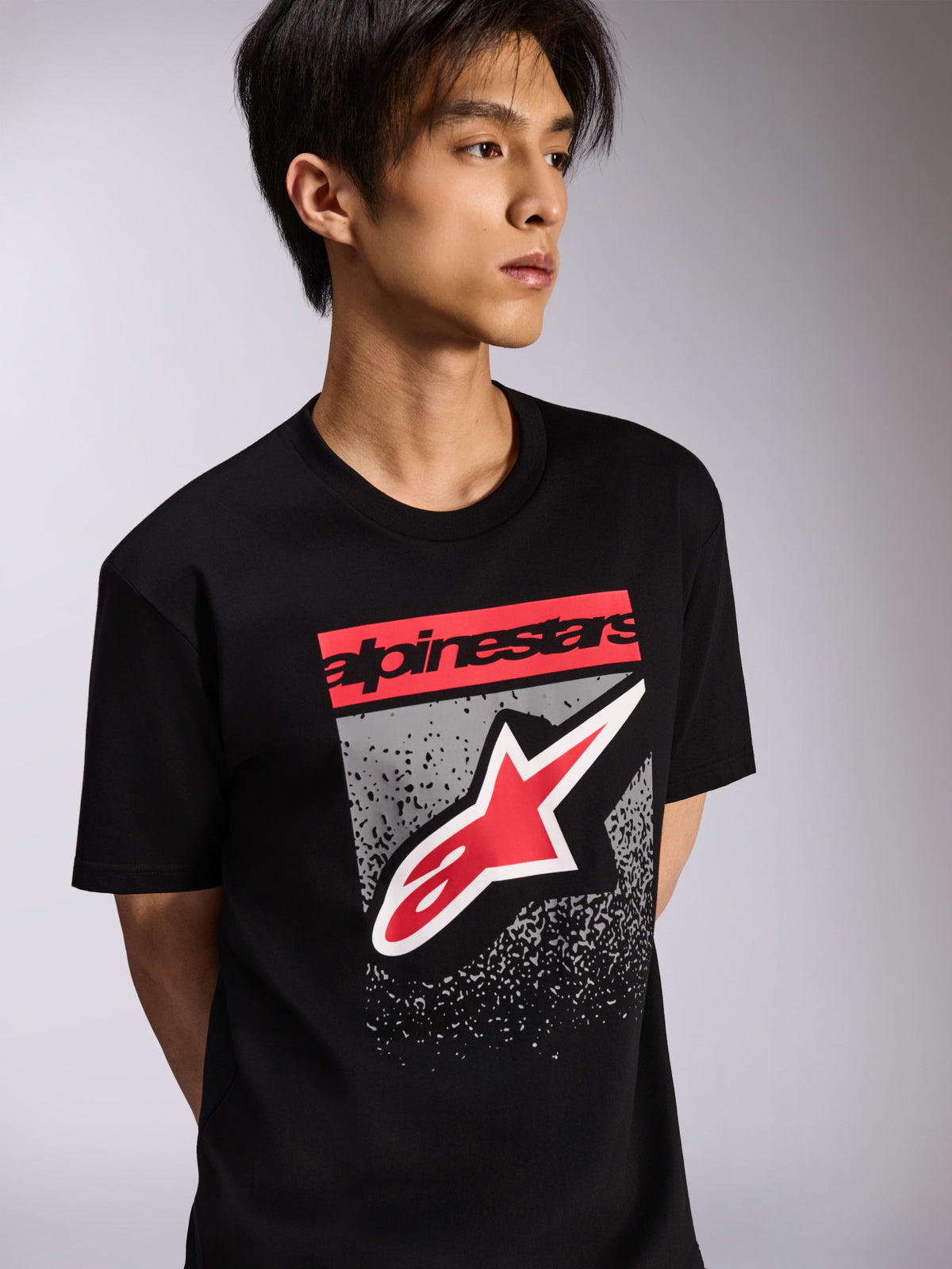 Alpinestars Noka CSF Tee, kurzärmeliges T-Shirt, Schwarz, mit rotem Branding-Block und großem rot-weißen Astars-Logo auf grau strukturiertem Hintergrund, lässige Motorsport-Streetwear
