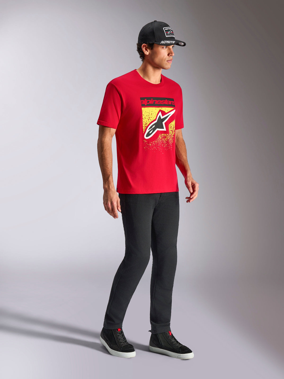 Alpinestars Noka CSF Tee, T-shirt met korte mouwen, rood, met Astars-logo aan de voorkant met MX-verloop op een gele graphic, gedragen met een zwarte Alpinestars-pet en zwarte broek, casual motorsport streetwear