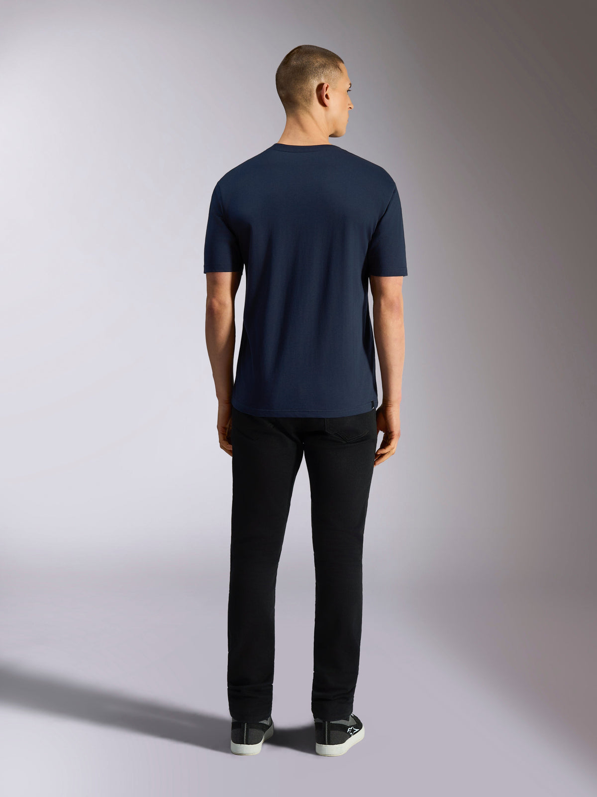 Alpinestars Noka CSF Tee, t-shirt à manches courtes, bleu marine, vue arrière d'un homme portant le t-shirt avec un pantalon noir et des baskets, streetwear décontracté motorsport