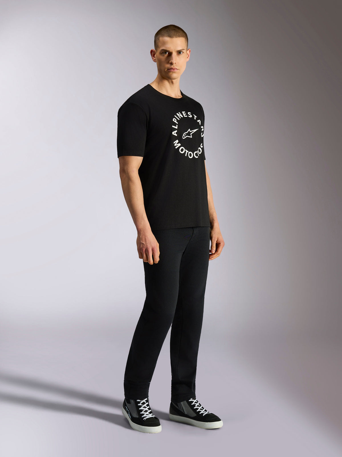 Alpinestars MX CSF Tee, t-shirt à manches courtes, noir, graphique Alpinestars Motocross circulaire blanc sur la poitrine, porté par un mannequin avec un pantalon noir et des baskets, streetwear décontracté inspiré des sports mécaniques