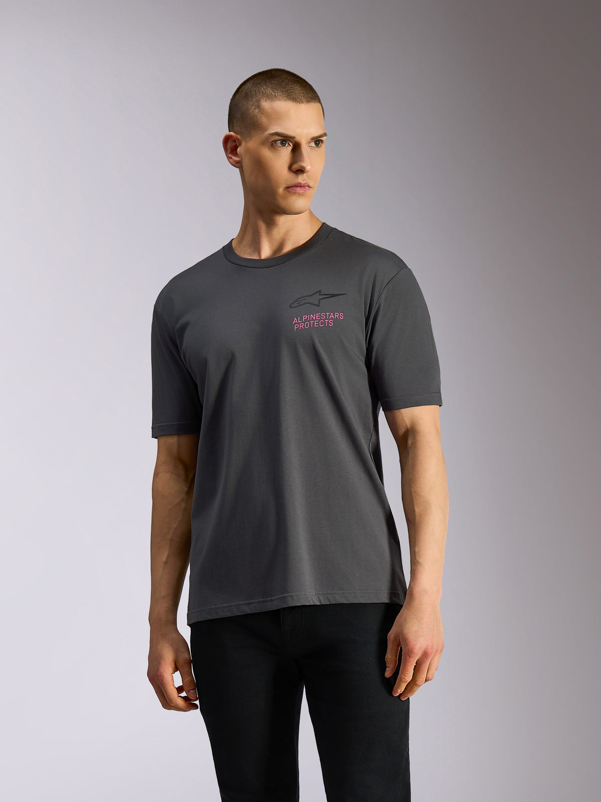 Alpinestars Pop Helmet CSF Tee, T-shirt met korte mouwen, antracietgrijs, gedragen door model, met zwart Astars-logo en roze 'ALPINESTARS PROTECTS' tekst op de borst, casual motorsport streetwear