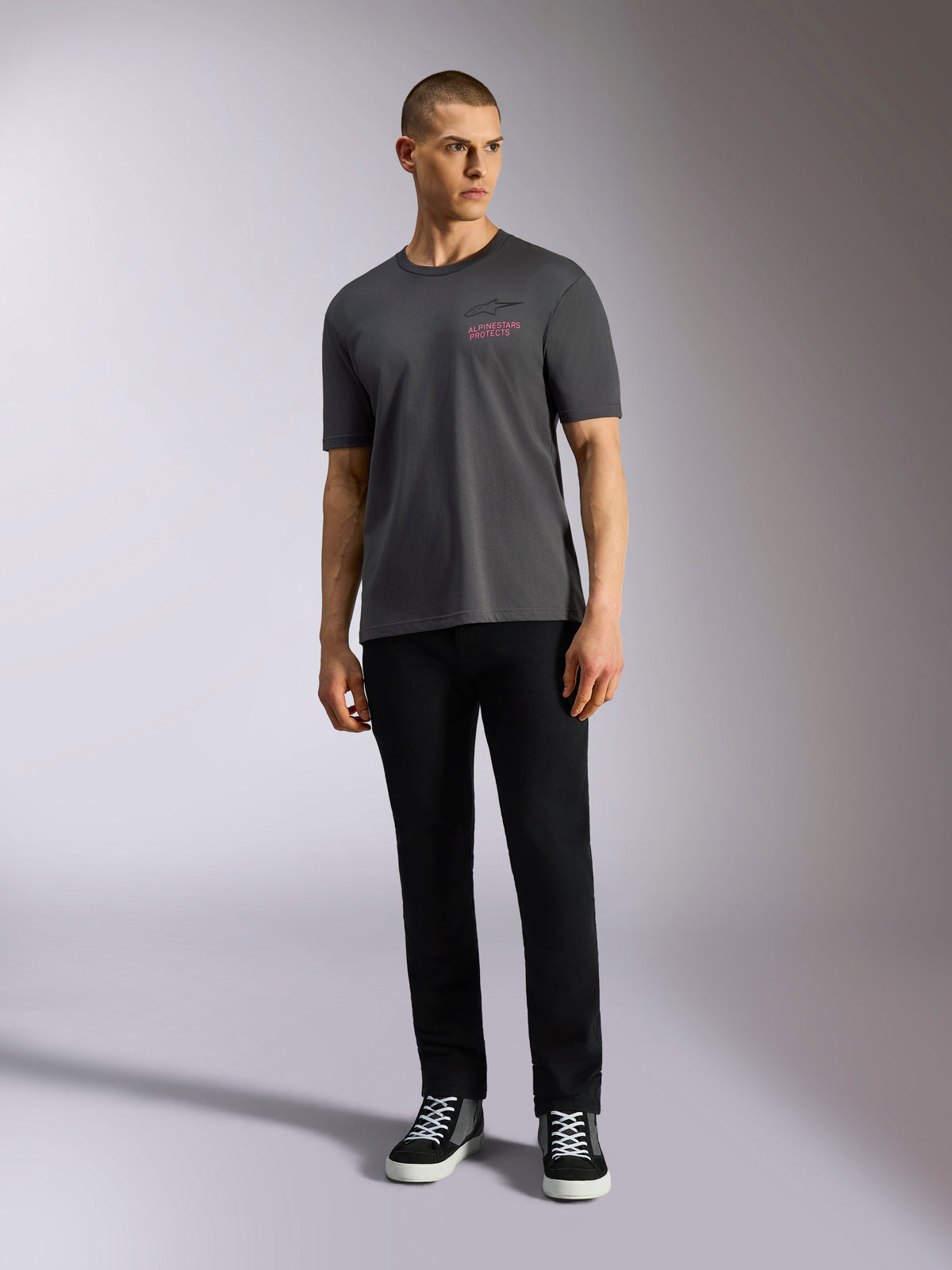 Alpinestars Pop Helmet CSF Tee, T-shirt met korte mouwen, antracietgrijs, met een roze Alpinestars-logo op de borst, gedragen door een mannelijk model met zwarte broek en sneakers, casual motorsport streetwear