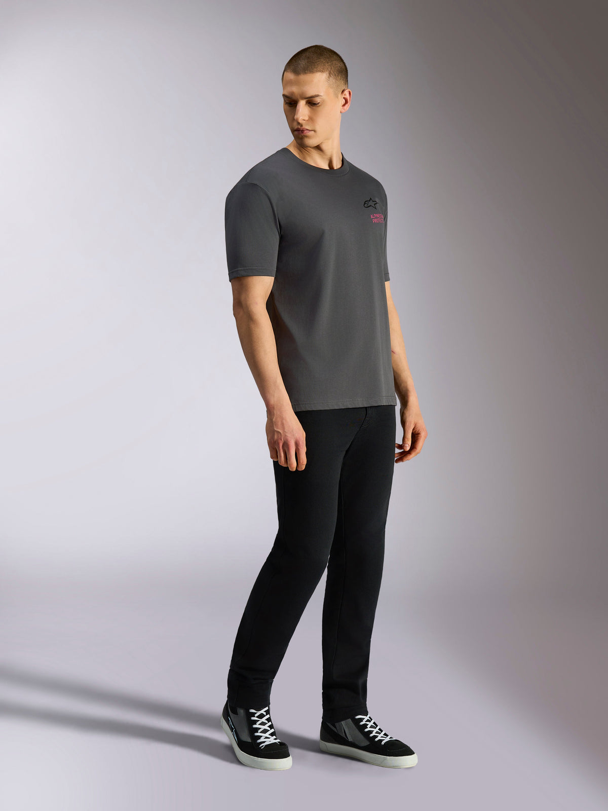 Alpinestars Pop Helmet CSF Tee, T-shirt met korte mouwen, antracietgrijs, gedragen door model met zwarte broek en sneakers, voorzien van zwart Astars-logo en roze belettering op de voorzijde, casual motorsport streetwear