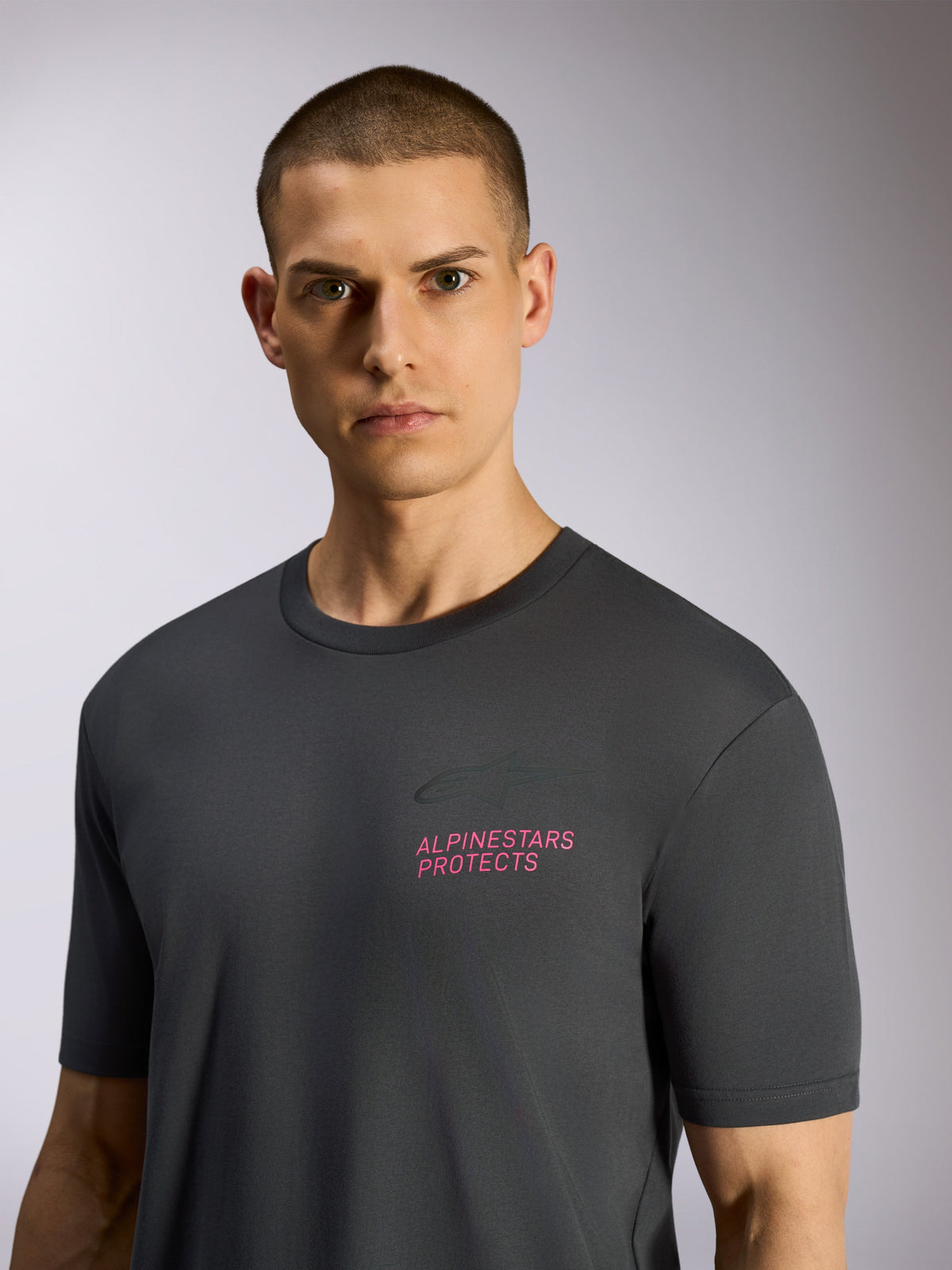 Alpinestars Pop Helmet CSF Tee, T-shirt met korte mouwen, antracietgrijs, gedragen door model, voorzien van roze 'ALPINESTARS PROTECTS' tekst en Astars-logo op de borst, casual motorsport streetwear