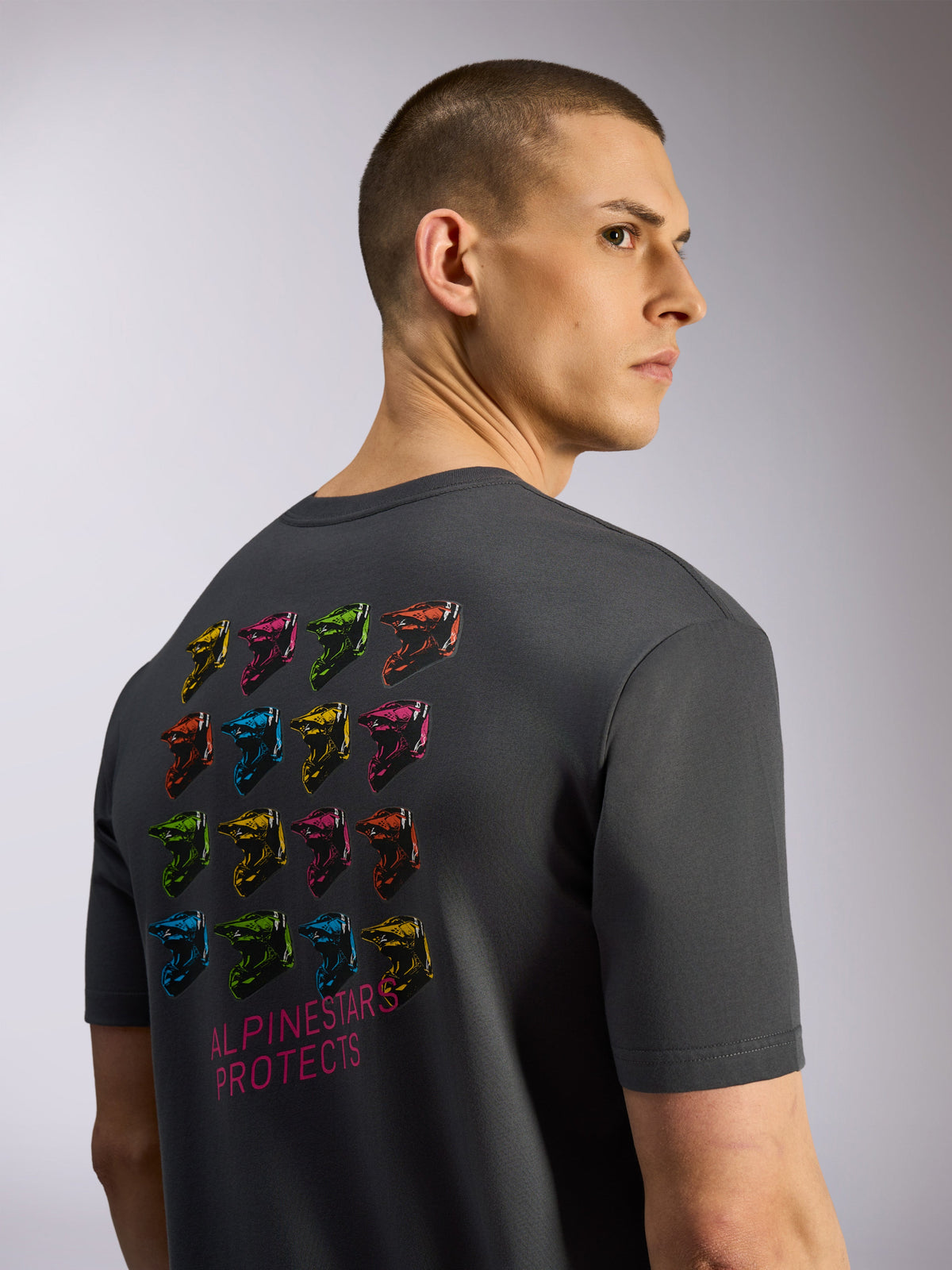 Alpinestars Pop Helmet CSF Tee, T-shirt met korte mouwen, antracietgrijs, achteraanzicht met een grid van kleurrijke M10-helmen en 'Alpinestars Protects' tekst, casual motorsport streetwear