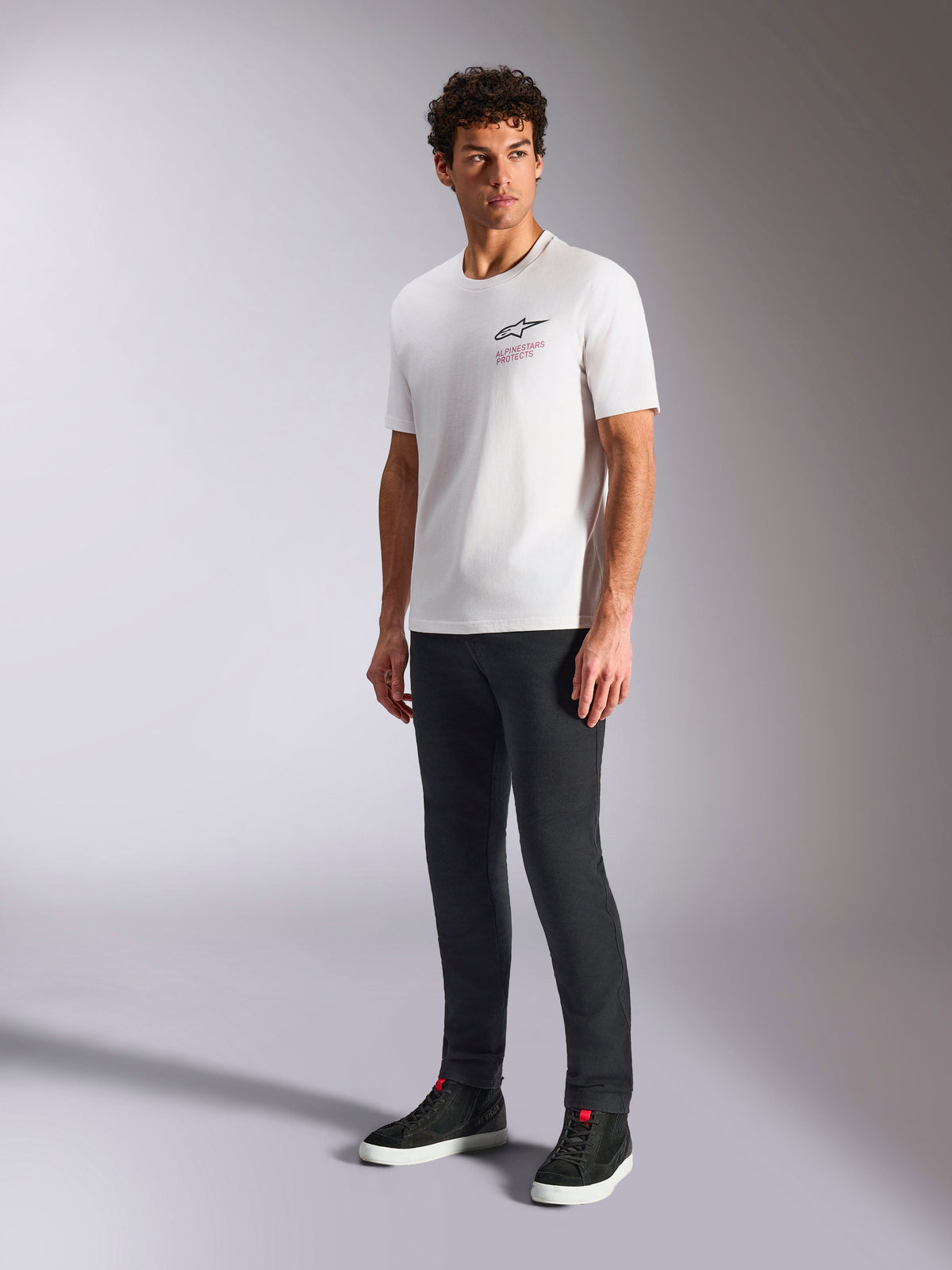 T-shirt Alpinestars Pop Helmet CSF, t-shirt à manches courtes, blanc, avec logo Astars et texte rouge à l'avant, porté par un mannequin homme avec un pantalon sombre et des baskets noires, streetwear motorsport décontracté