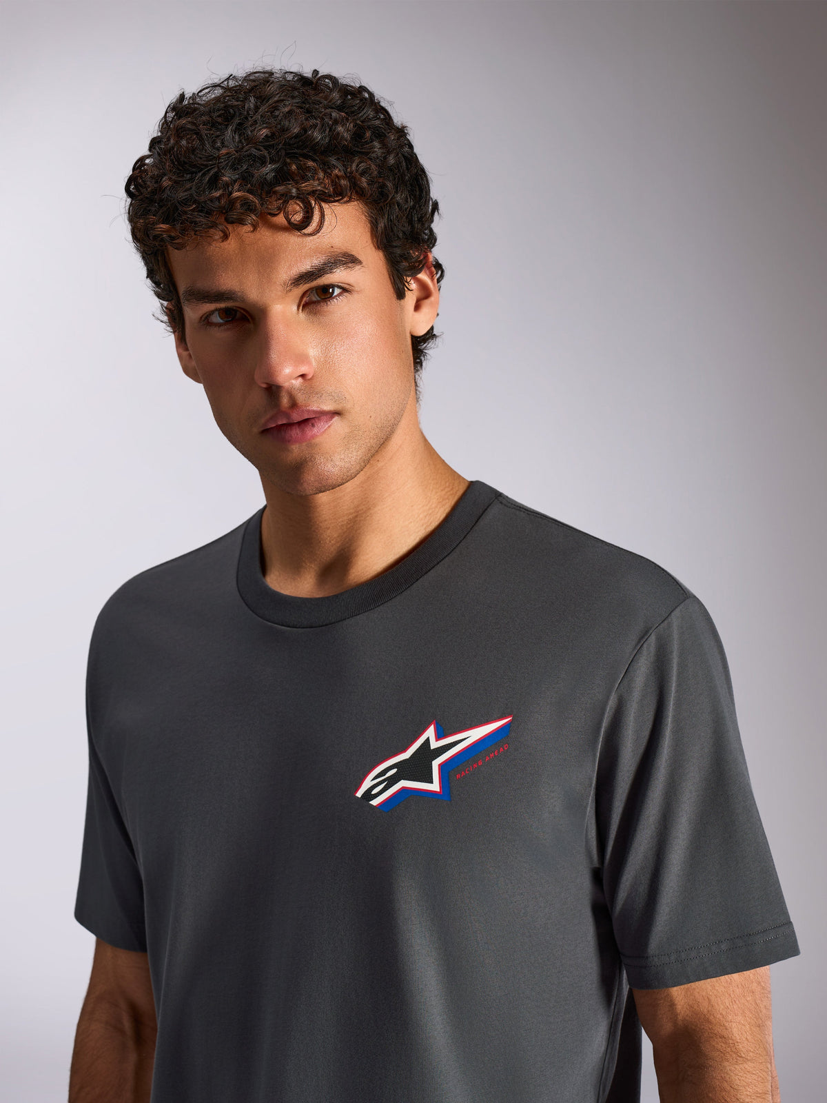 Alpinestars Angler CSF Tee, Kurzarm-T-Shirt, Anthrazit, getragen von einem männlichen Model, mit einem mehrfarbigen Astars-Logo auf der Brust, lässige Motorsport-Streetwear