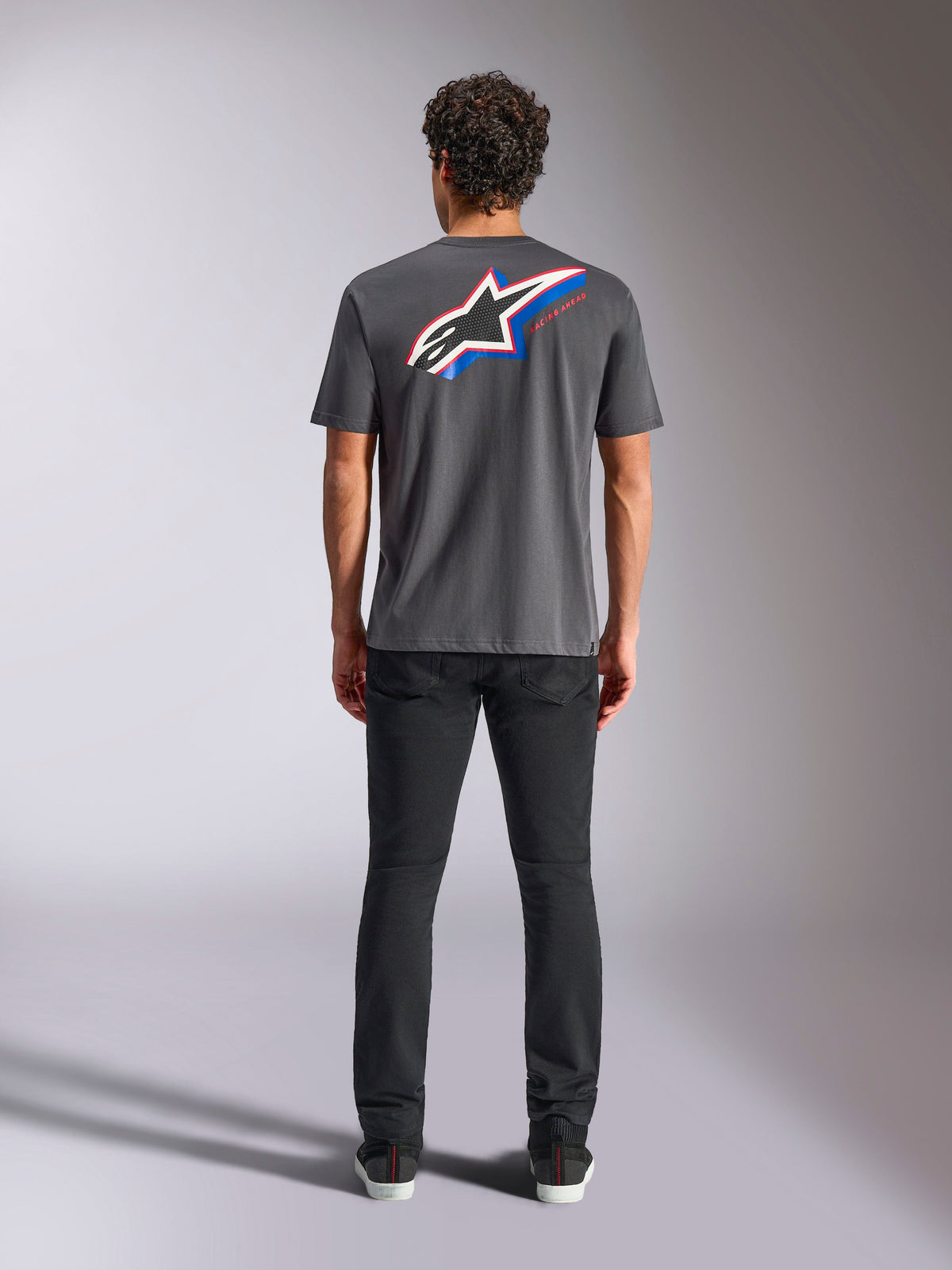 Alpinestars Angler CSF Tee, Kurzarm-T-Shirt, Charcoal, Großes mehrfarbiges Astars-Logo auf der Rückseite mit roten und blauen Akzenten, Rückansicht am Model, lässige Motorsport-Streetwear