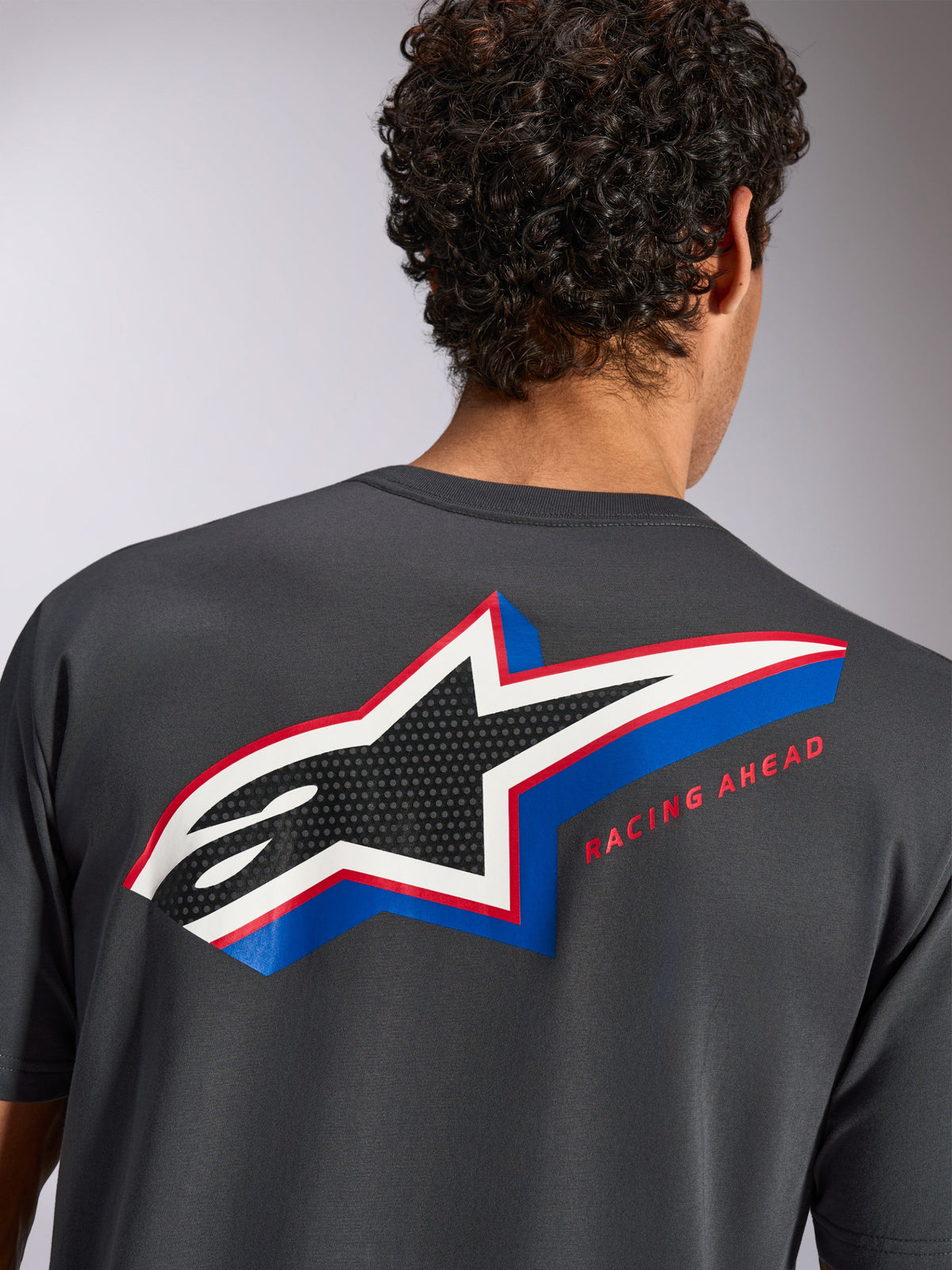 Alpinestars Angler CSF Tee, Kurzarm-T-Shirt, Anthrazit, Rückansicht am Modell mit großem mehrfarbigem Alpinestars Stern-Logo, perforierter Füllung und „RACING AHEAD“-Schriftzug, lässige Motorsport-Streetwear
