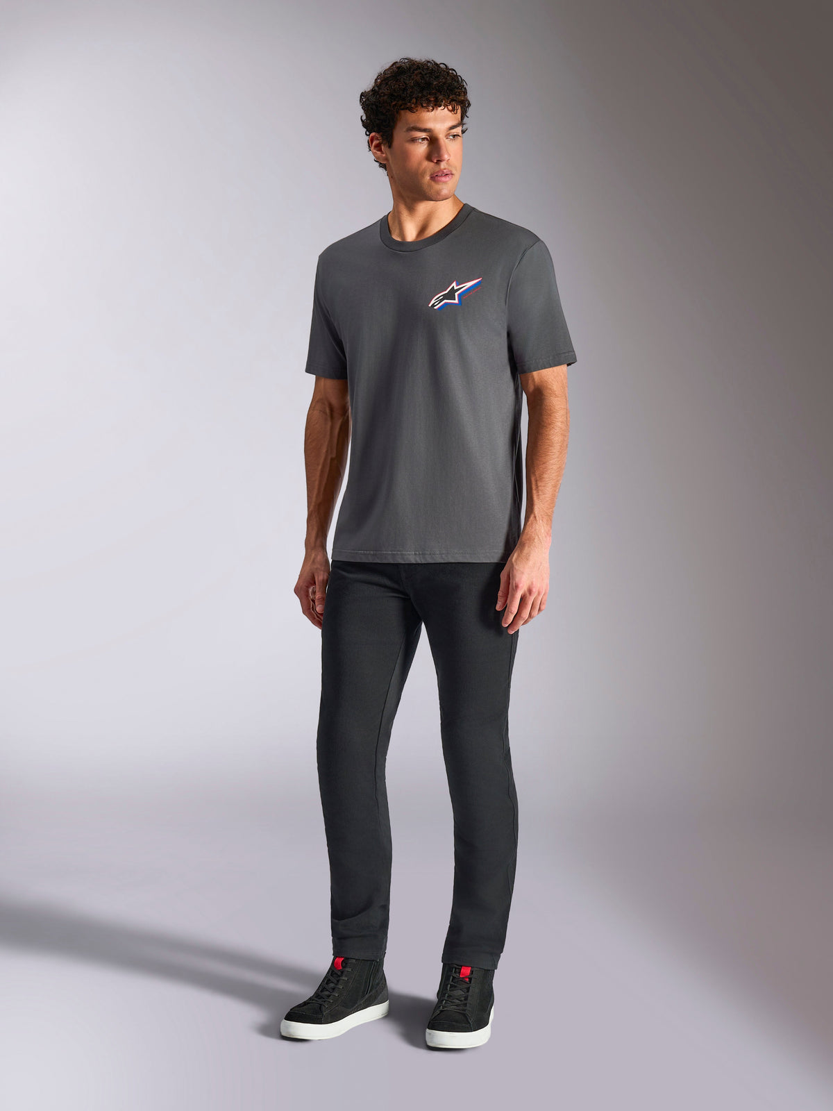 Alpinestars Angler CSF T-Shirt, Kurzarm-T-Shirt, Charcoal, mehrfarbiges Astars-Logo auf der Brust, getragen mit schwarzer Hose und Sneakern, lässige Motorsport-Streetwear
