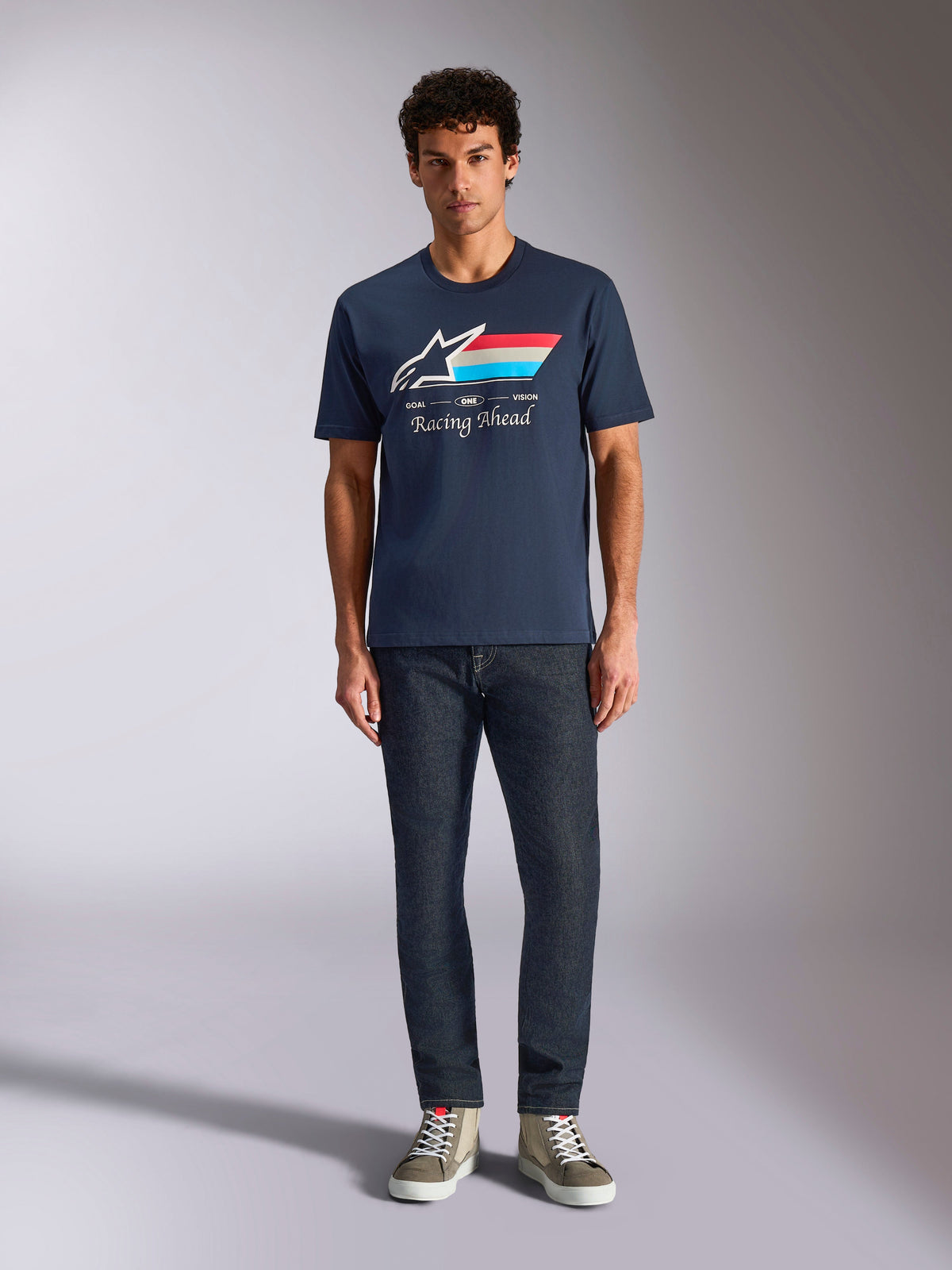 Alpinestars Trifecta CSF Tee, Kurzarm-T-Shirt, Marineblau, weißes Astars-Logo mit rot-weiß-hellblauen Streifen und „Racing Ahead“-Schriftzug, getragen mit dunkler Jeans und olivgrünen Sneakern, lässige Motorsport-Streetwear