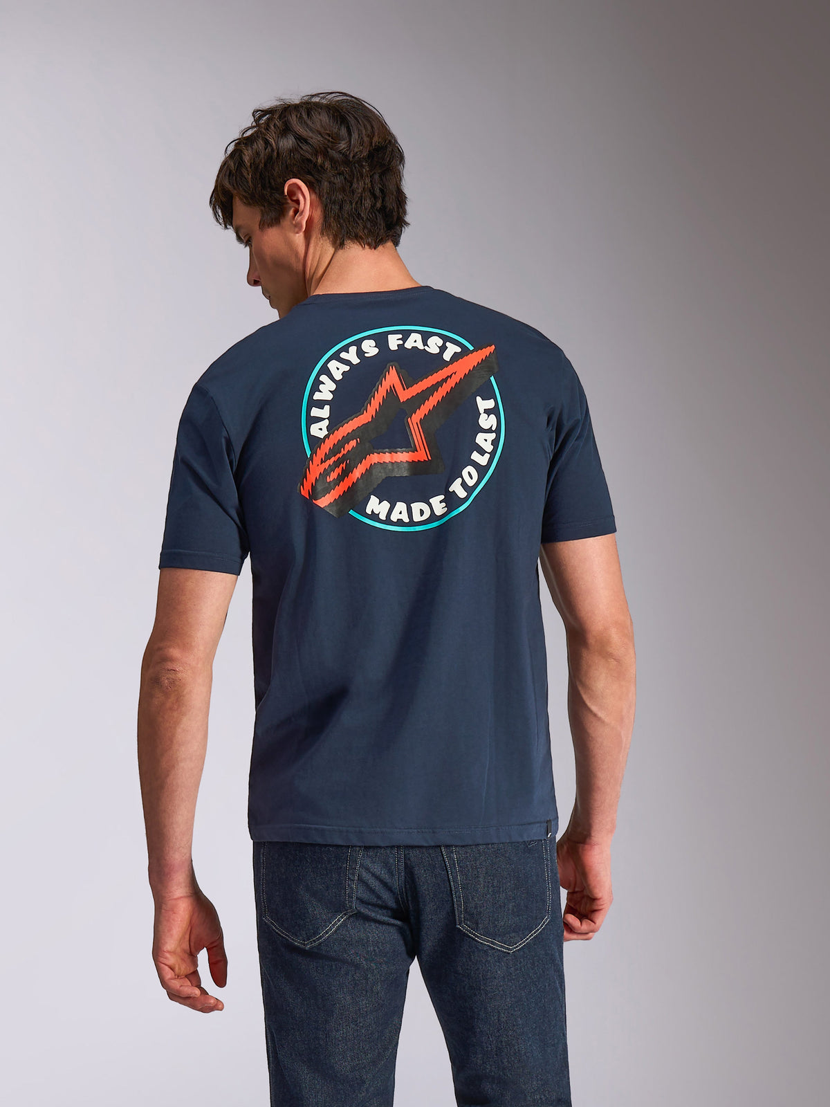 Alpinestars Aorbit CSF Tee, T-shirt met korte mouwen, navy blauw, achteraanzicht op model met ronde 'Always Fast Made to Last' graphic en rood Astars-logo, casual motorsport-geïnspireerde streetwear