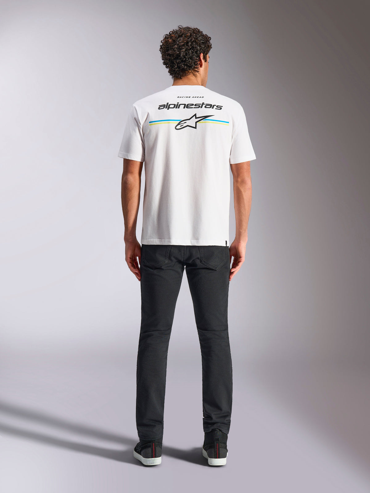 Alpinestars Lanes CSF Tee, T-shirt à manches courtes, blanc, vue de dos sur modèle présentant le logo Alpinestars et l'étoile Astars sur des rayures horizontales bleues et jaunes, streetwear motorsport décontracté