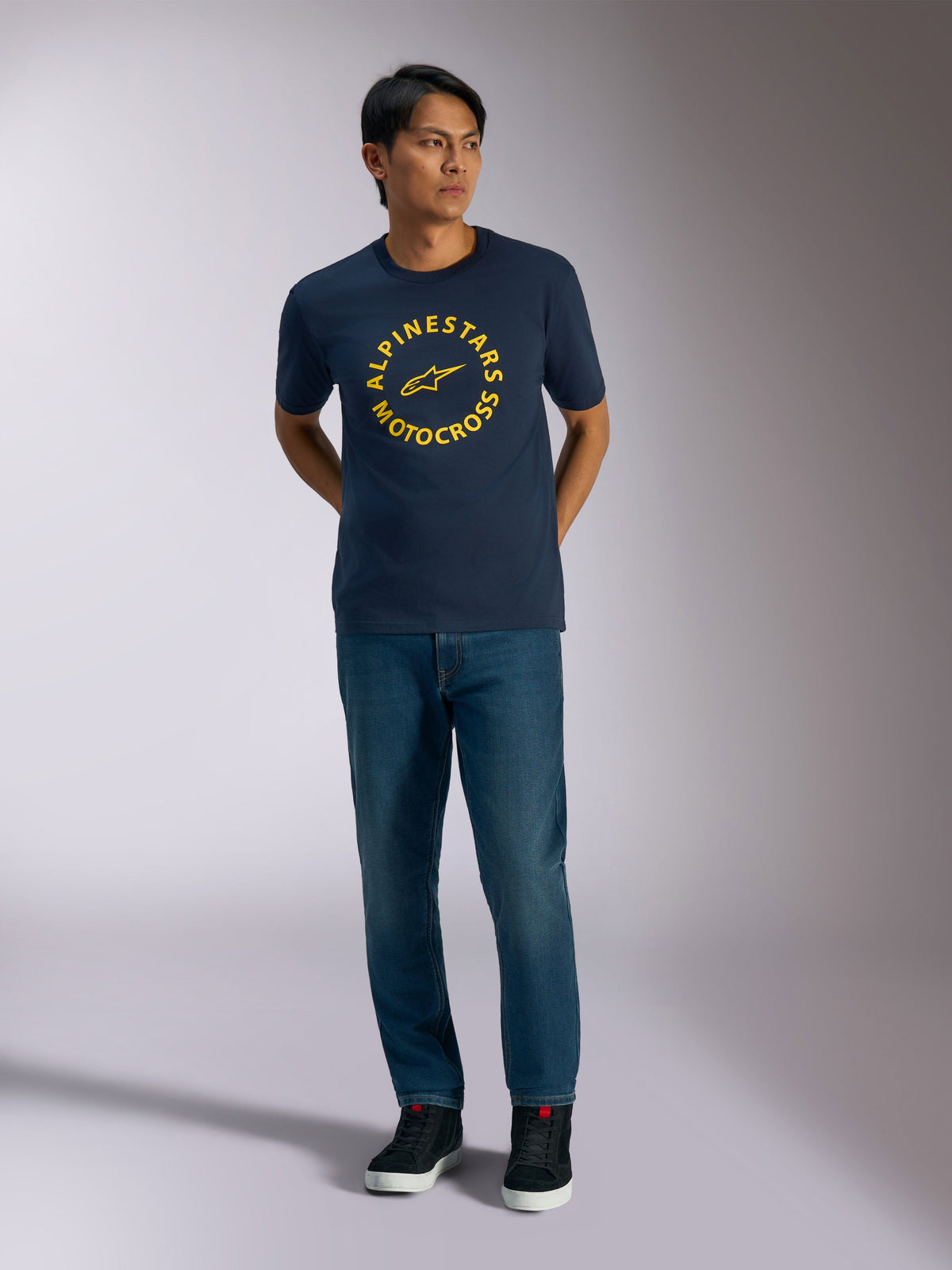 Alpinestars MX CSF Tee, T-shirt met korte mouwen, marineblauw, met een gele cirkelvormige Alpinestars Motocross-graphic, gedragen door een model met blauwe jeans en zwarte sneakers, casual motorsport streetwear