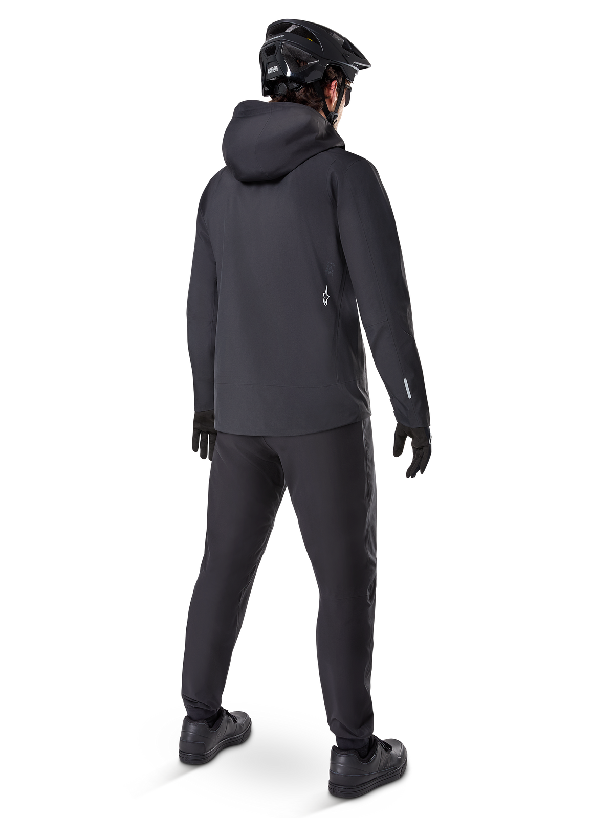 Alpinestars A-Dura Elite Waterdichte Jas, Zwart, achteraanzicht met capuchon over de helm en een verlengde achterzoom, gecombineerd met bijpassende zwarte MTB-broek, handschoenen en helm voor volledige trailbescherming in alle weersomstandigheden.