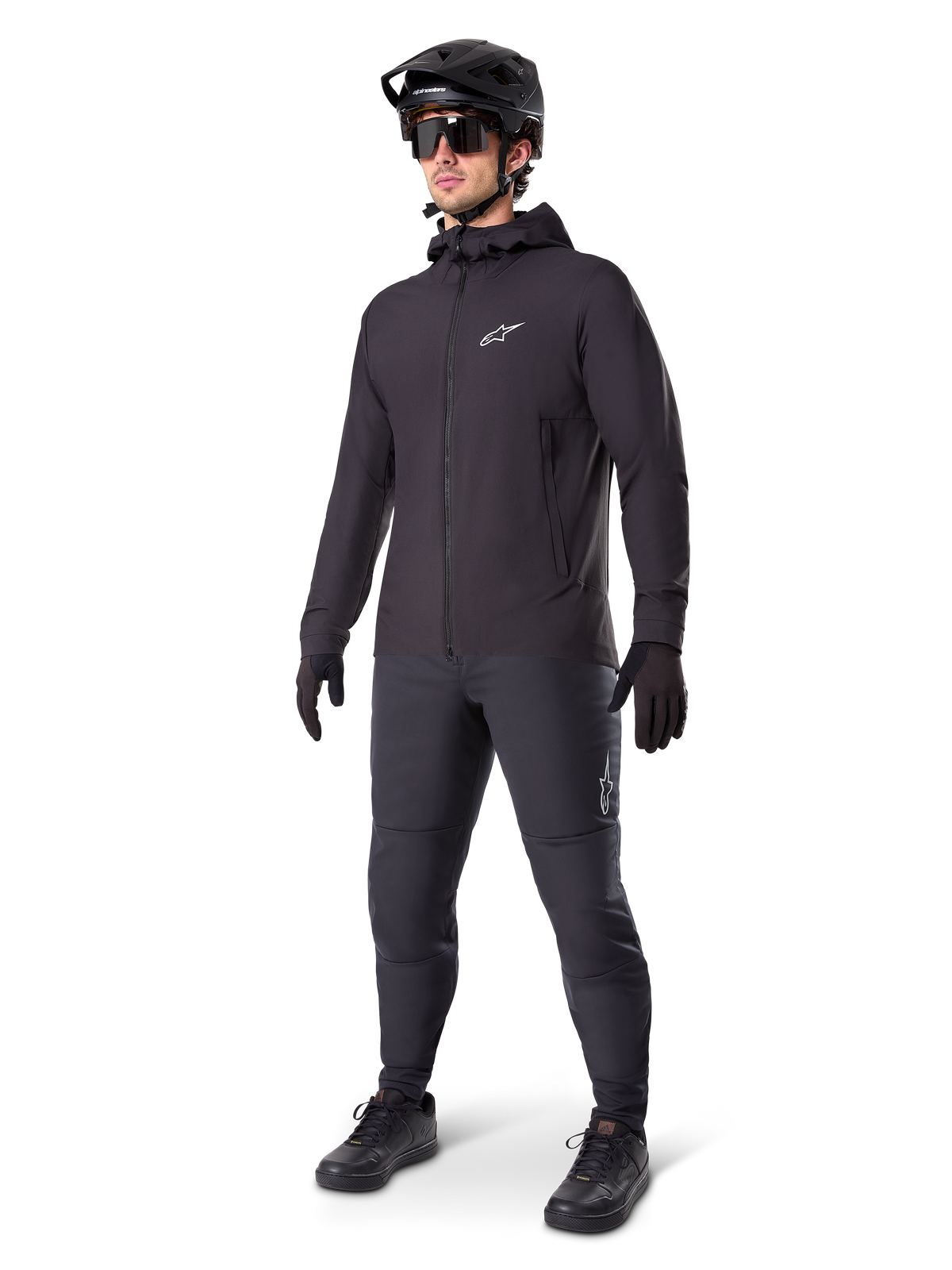 Veste thermique Alpinestars A-Dura en noir, portée par un cycliste avec un équipement complet de VTT incluant un casque noir, des lunettes de soleil et un pantalon de cyclisme, veste à capuche isolante et légère pour la performance à vélo par temps froid.