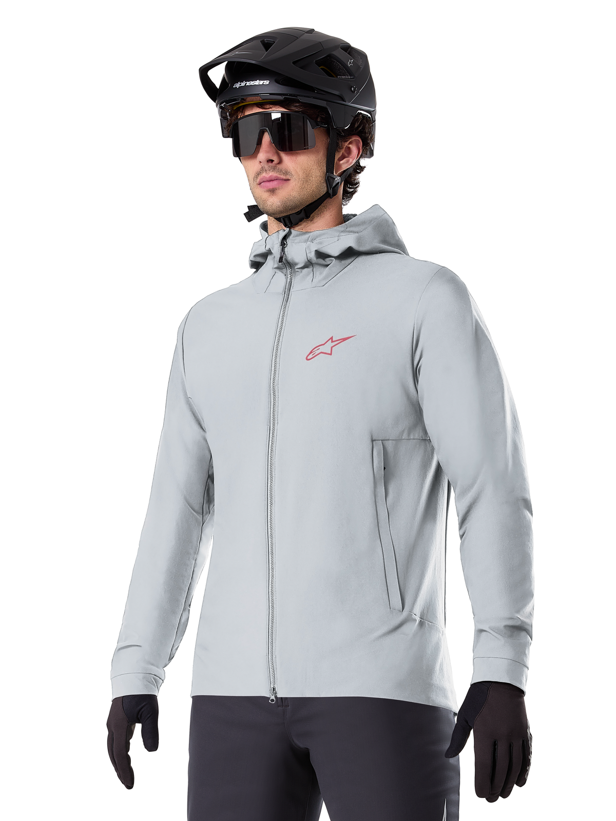 Veste thermique Alpinestars A-Dura, veste de cyclisme isolante gris clair, design à capuche avec petit logo rouge, portée avec un casque et des gants noirs, vêtement technique de VTT pour rouler par temps froid