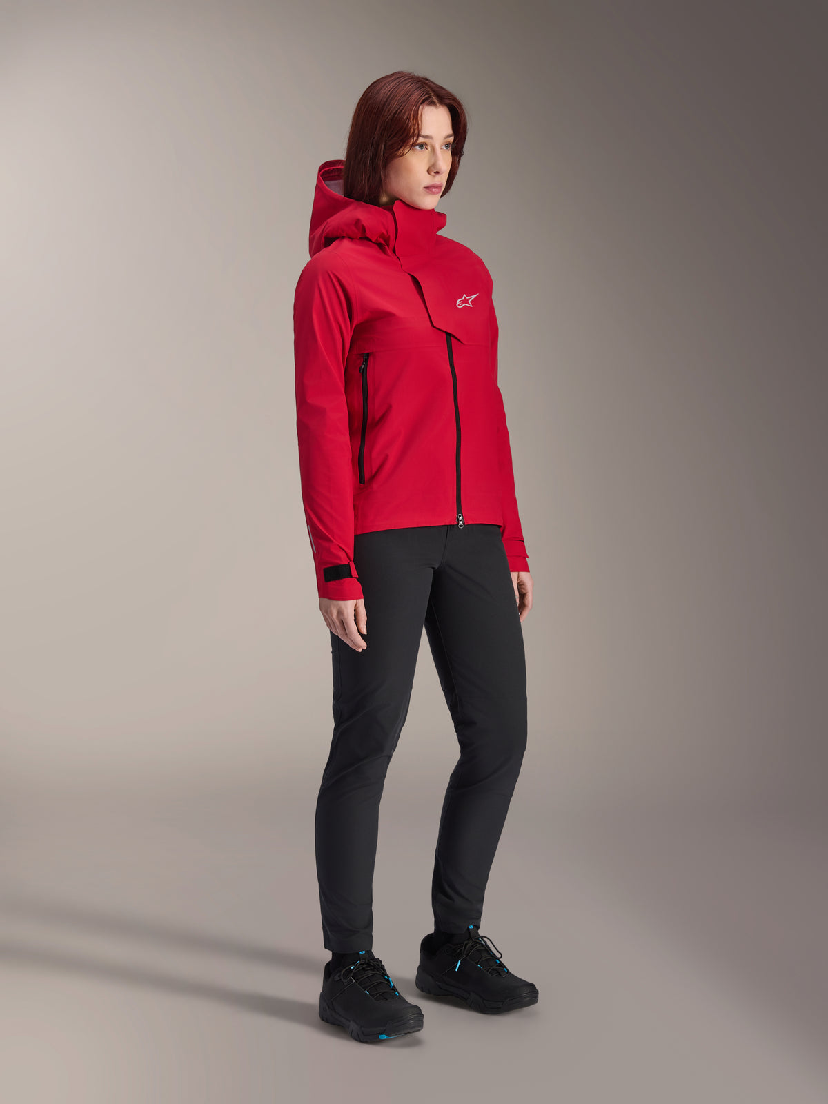 Veste imperméable Alpinestars Stella A-Dura Elite pour femme, Rouge Fluo, veste de pluie de VTT à capuche avec logo Astars blanc sur le rabat de poitrine, portée avec un pantalon noir et des chaussures de VTT noires, équipement de performance technique pour le trail